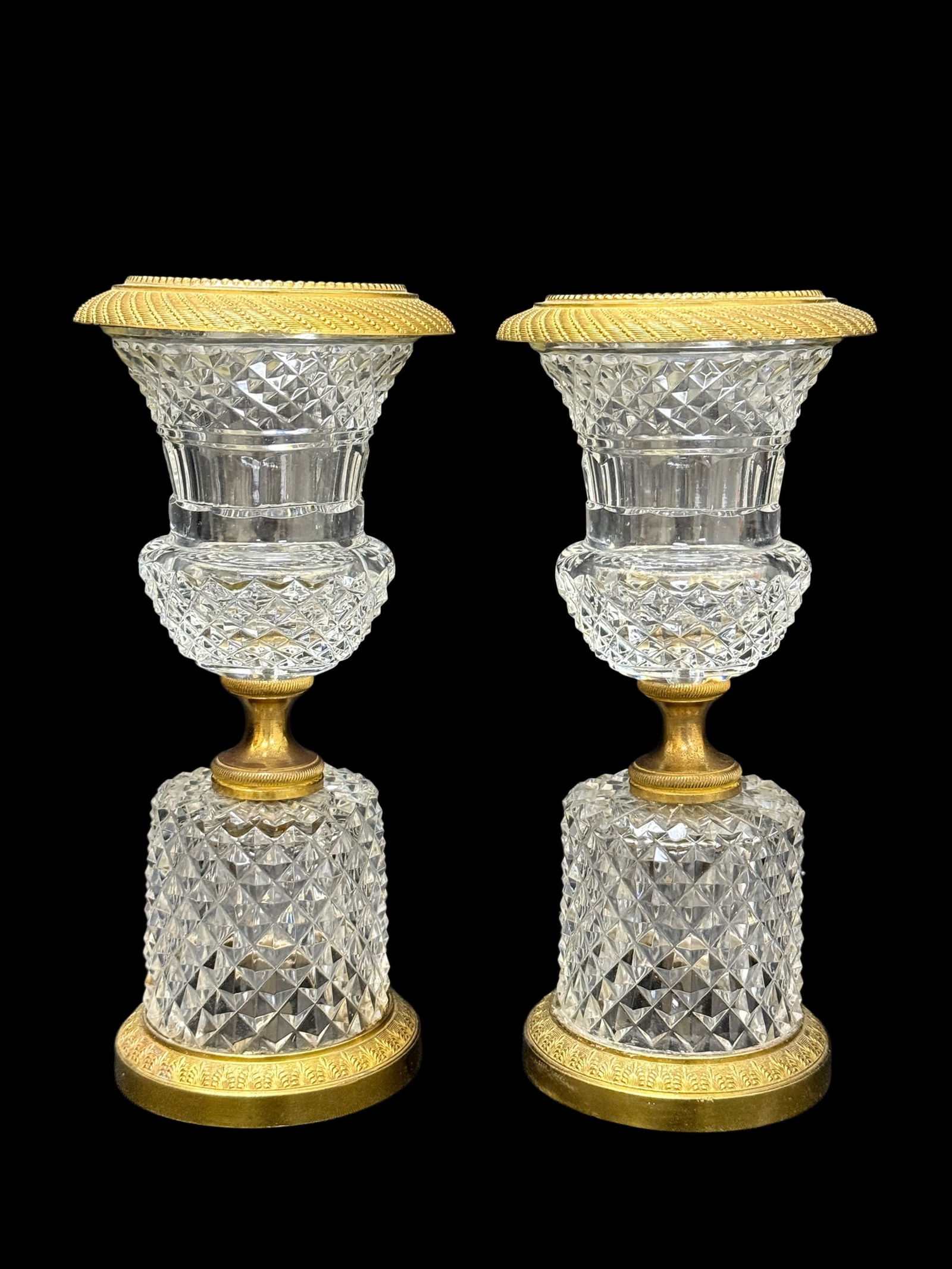 Early 20th C. French Gilt Bronze & Crystal Urns, Pair: Elegant pair of French urn-form vessels crafted in richly detailed gilt bronze and finely cut crystal, dating to the early 20th century, each featuring a flared gilt bronze rim with intricate engine-t