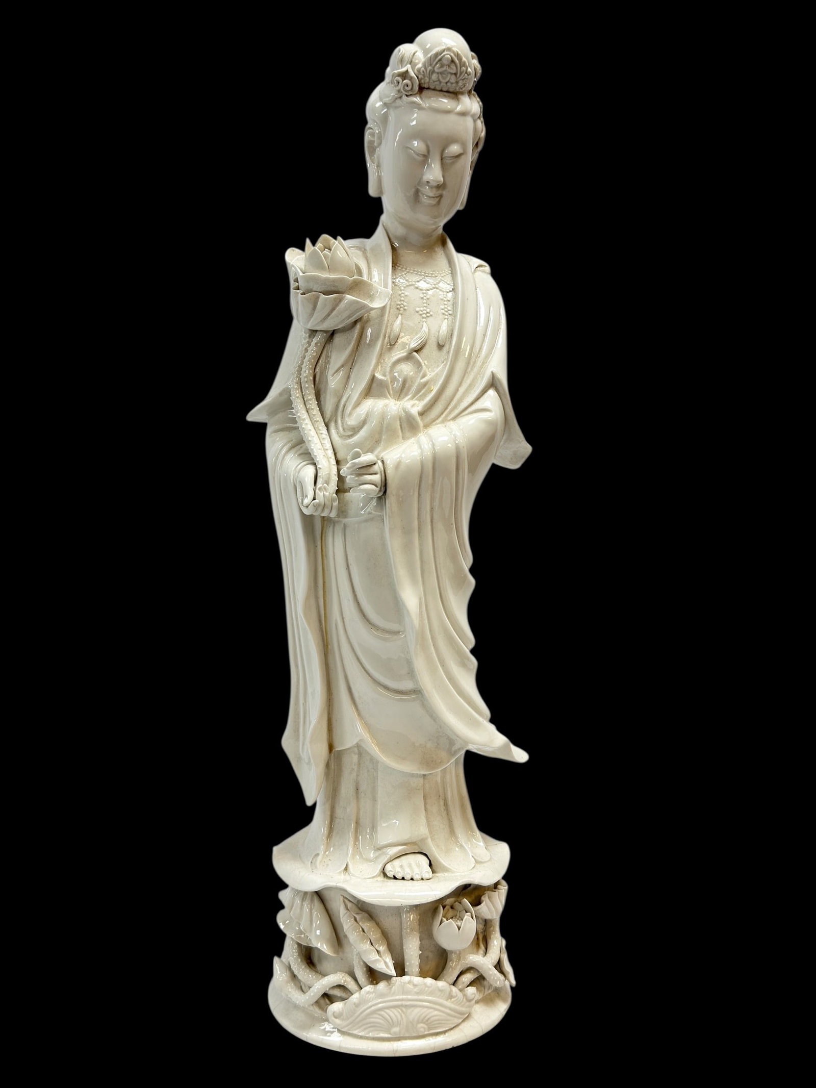 Mid-20th C. Chinese Blanc de Chine Style Porcelain Figure of Guanyin: Mid-20th century Chinese blanc de Chine style porcelain figure depicting Guanyin, the Bodhisattva of Compassion, shown standing gracefully atop a lotus-form pedestal with scrolling lotus vines and blo