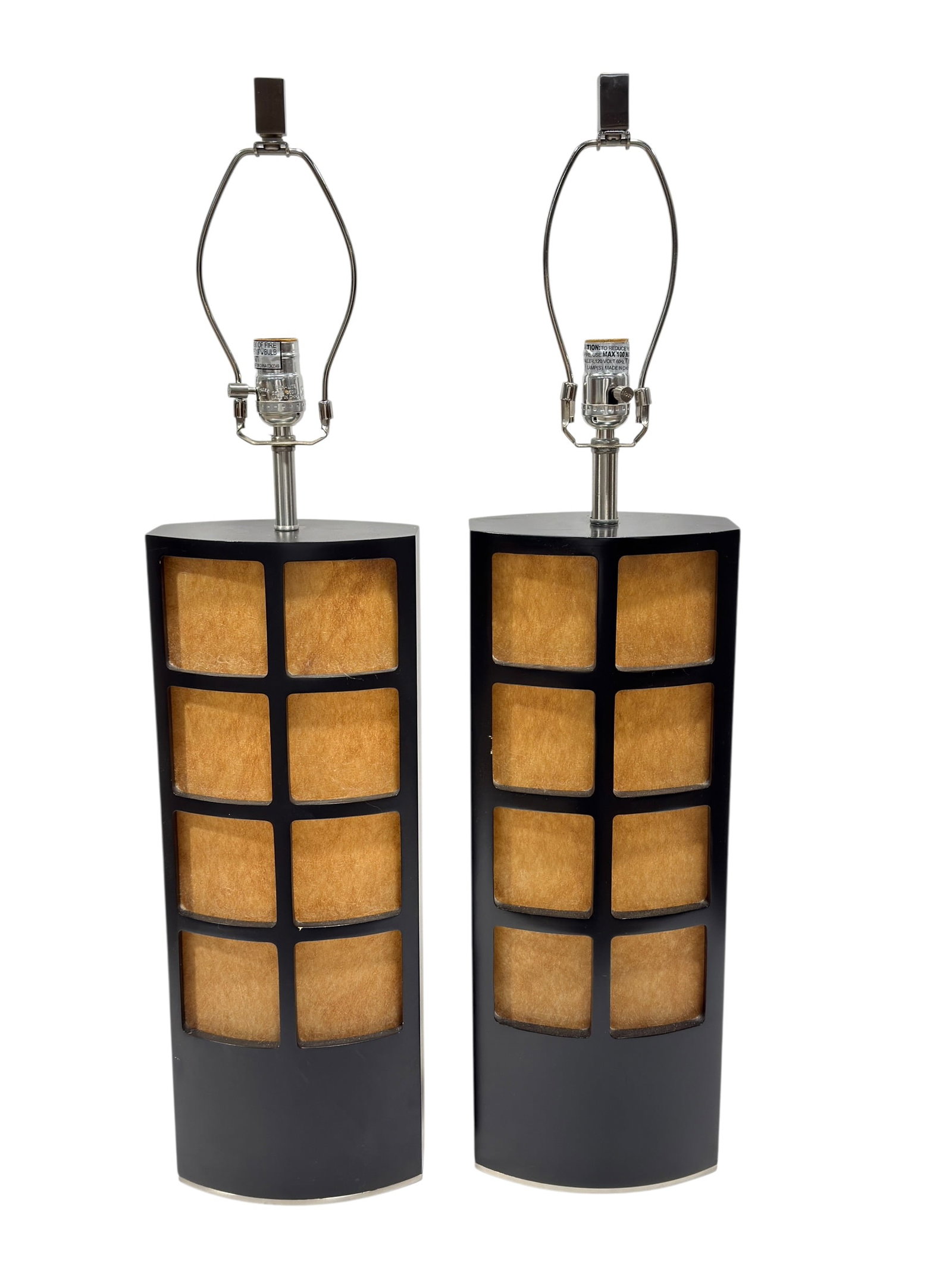 Japanese Style Black Panel Table Lamps, Pair: Striking pair of late 20th century Japanese style table lamps featuring tall faceted cylindrical bases in matte black with inset grid-form panels revealing warm textured tan inserts that softly diffus