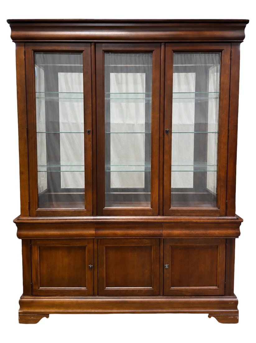 Broyhill Illuminated China Cabinet: Broyhill Illuminated China Cabinet / Breakfront in a rich medium-to-dark cherry finish featuring a molded crown above three framed glass display doors opening to adjustable glass shelving with integra