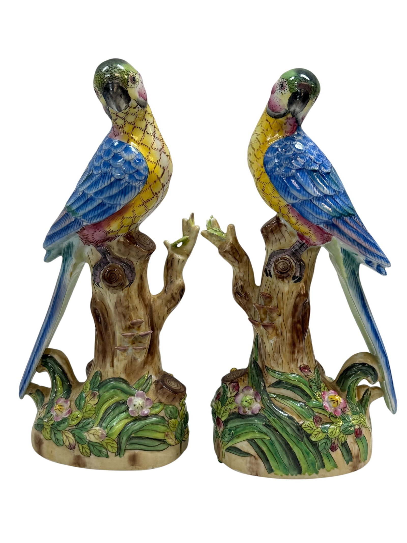 Pair of Andrea by Sadek Porcelain Parrot Figures: A decorative pair of Andrea by Sadek porcelain parrot figures, each modeled as a colorful blue-and-yellow parrot perched atop a naturalistic tree stump with molded flowers and foliage at the base.