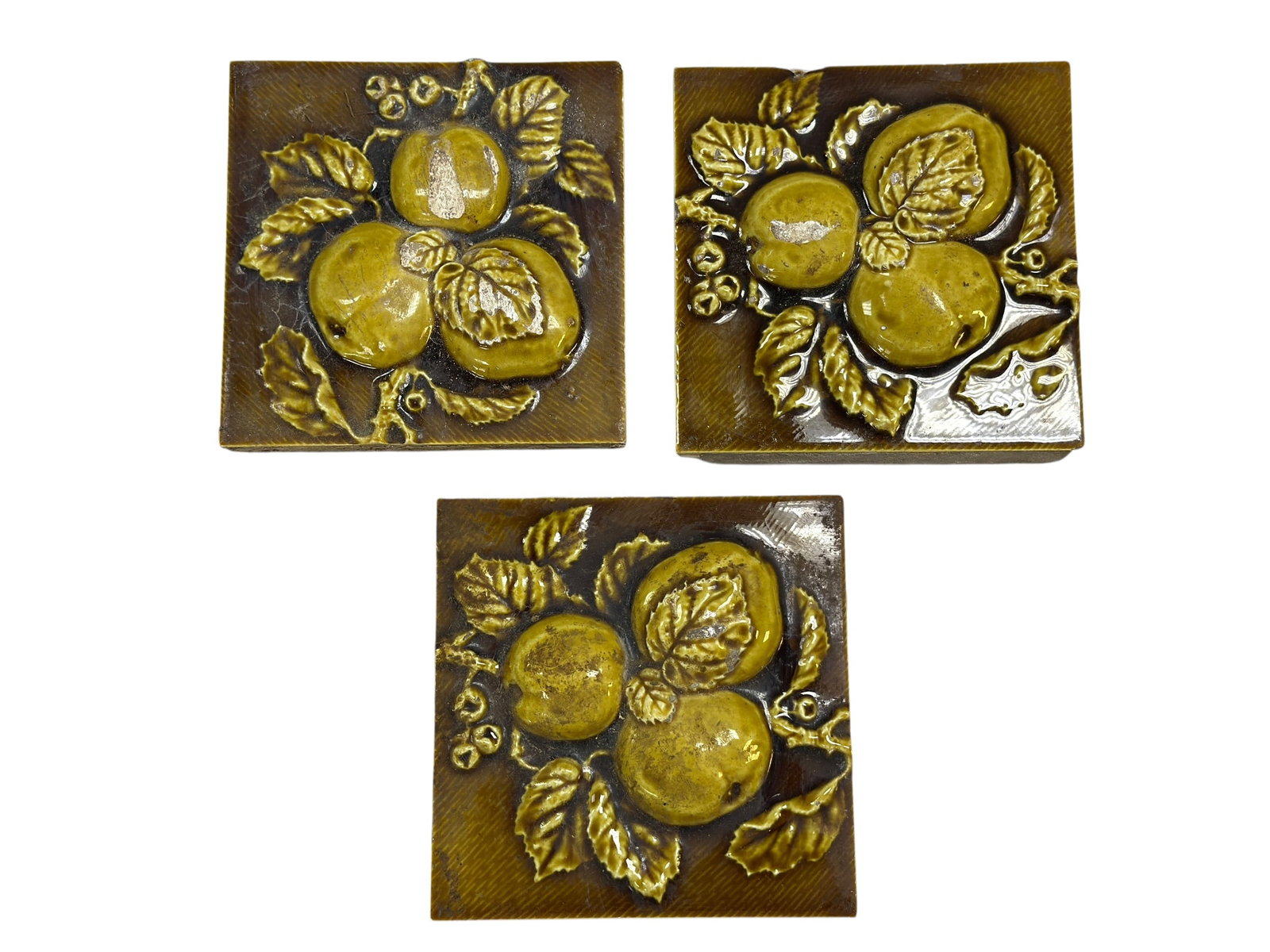 (3) Majolica-Style Fruit Relief Ceramic Tiles: A decorative set of three majolica-style ceramic wall tiles, each molded in high relief with apples, leaves, and berries, finished in rich olive green, brown, and golden glazes with a glossy surface