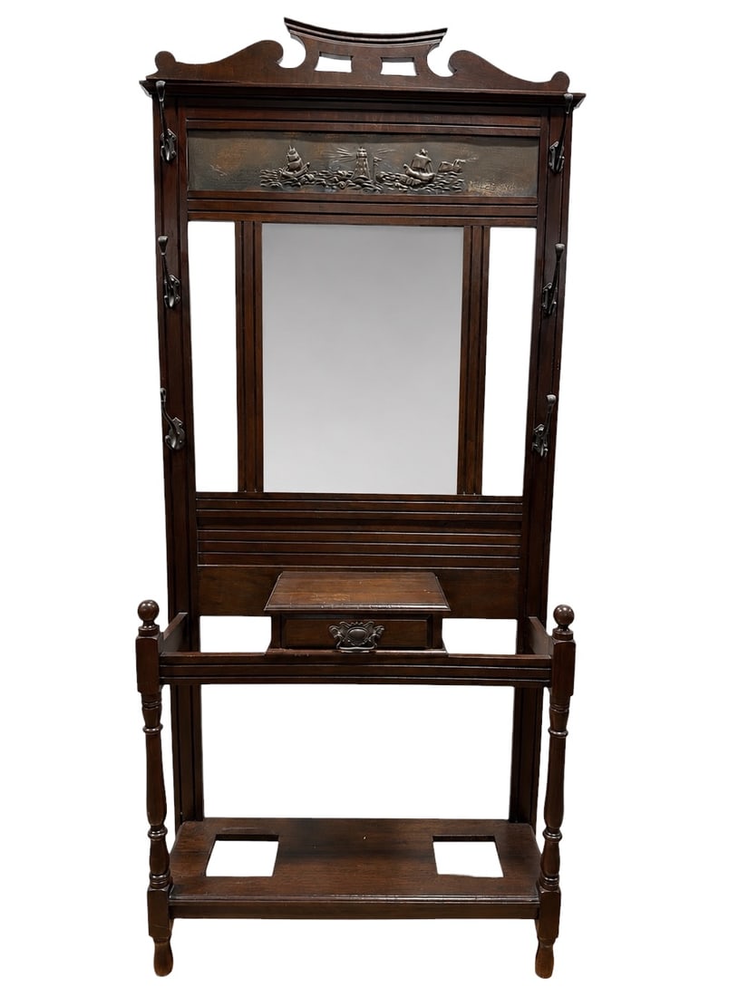Arts & Crafts Oak Hall Tree with Mirror: Arts & Crafts hall tree crafted in oak, featuring a shaped crest with decorative cutouts above a central embossed metal panel depicting a coastal scene with sailing ships and a lighthouse. The