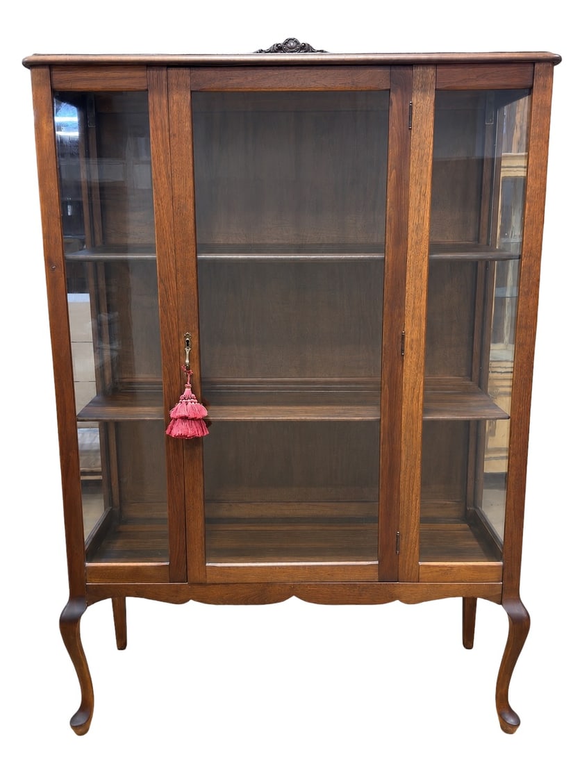 Early 20th Century Wood & Glass Display Cabinet: Early 20th-century wood display cabinet or vitrine of tall rectangular form, designed with twin glazed front doors, glazed side panels, and a gently shaped gallery crest centered by a carved floral or