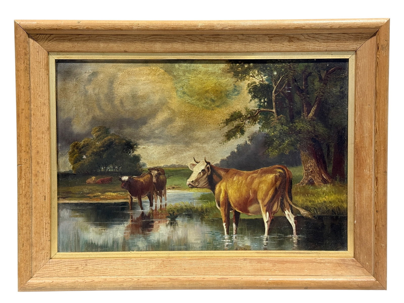 19th Century Pastoral Landscape with Cattle Watering, Oil on Canvas: A finely rendered 19th-century pastoral oil on canvas depicting cattle gathered in and around a tranquil woodland stream beneath a dramatic, cloud-filled sky. A large brown-and-white cow stands promin