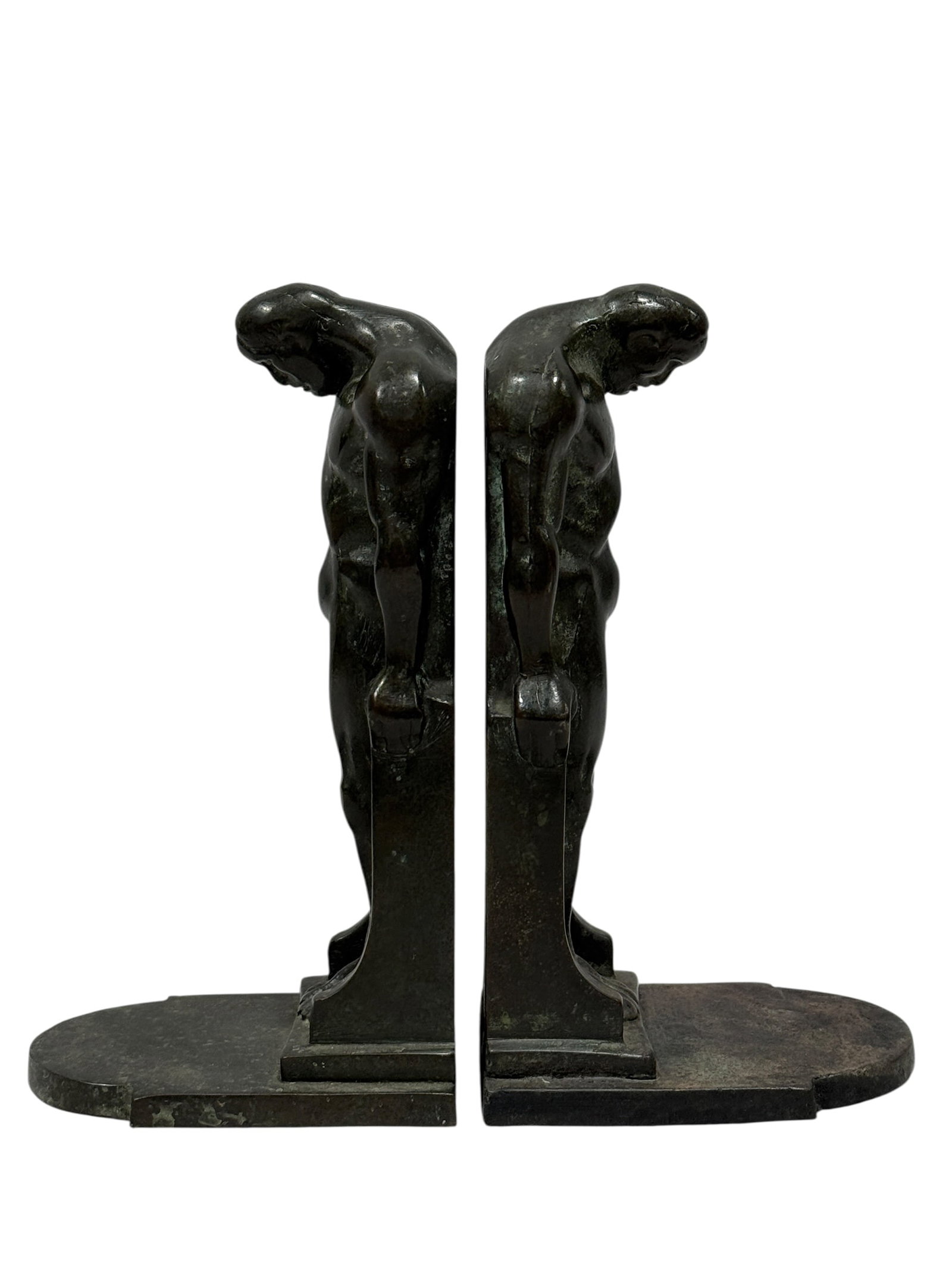 Early 20th Century Arts & Crafts Bronze Male Nude Bookends: Striking early 20th-century pair of patinated bronze figural bookends, each modeled as a muscular nude male figure standing in a pronounced forward-bending pose with head bowed, shoulders rounded, and