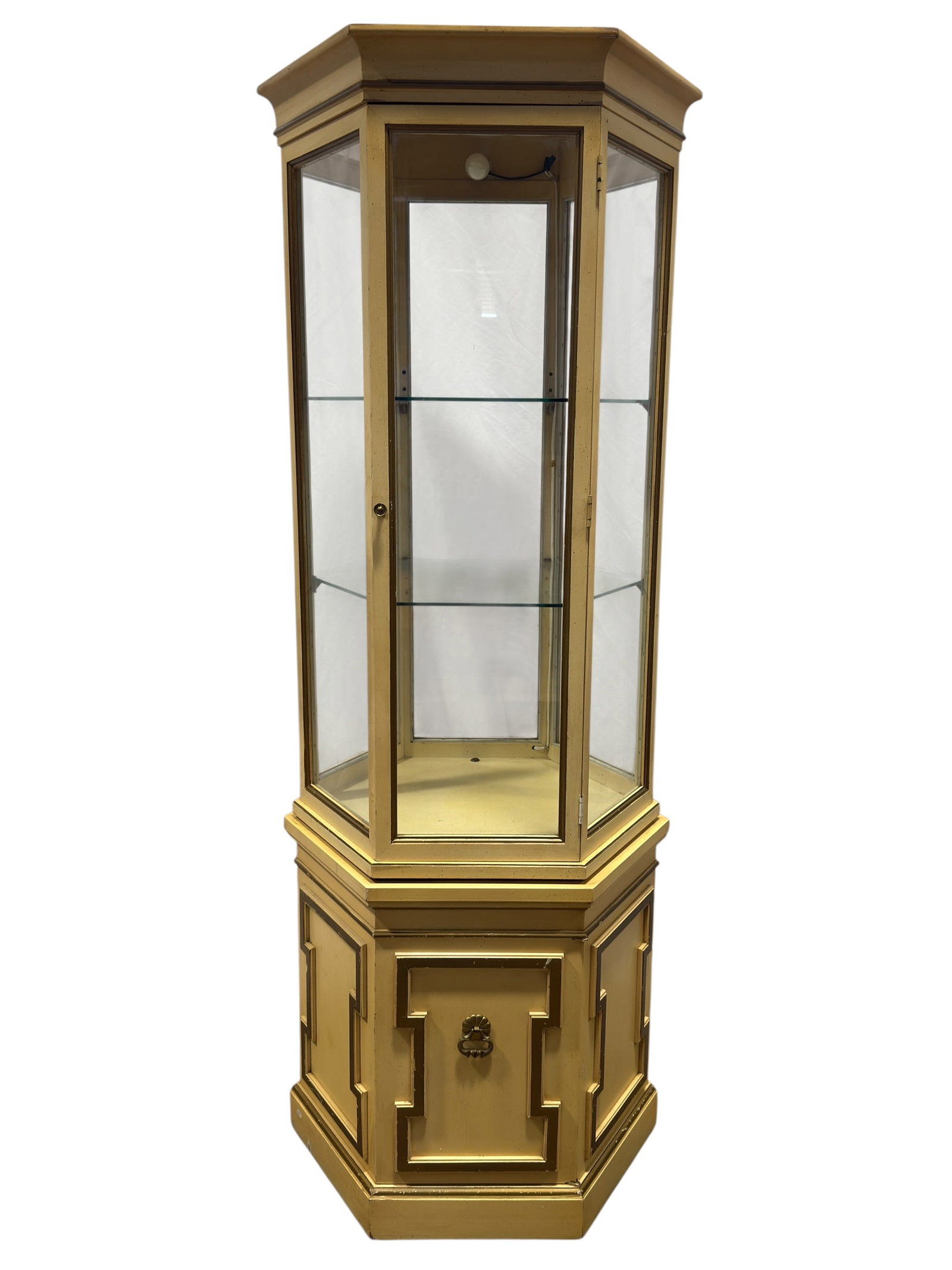 Vintage Hollywood Regency Style Illuminated Painted Curio Display Cabinet: Tall vintage illuminated display cabinet or vitrine in a Hollywood Regency / neoclassical decorative style, finished in a warm cream-gold painted surface with contrasting bronze-toned trim. The upper 