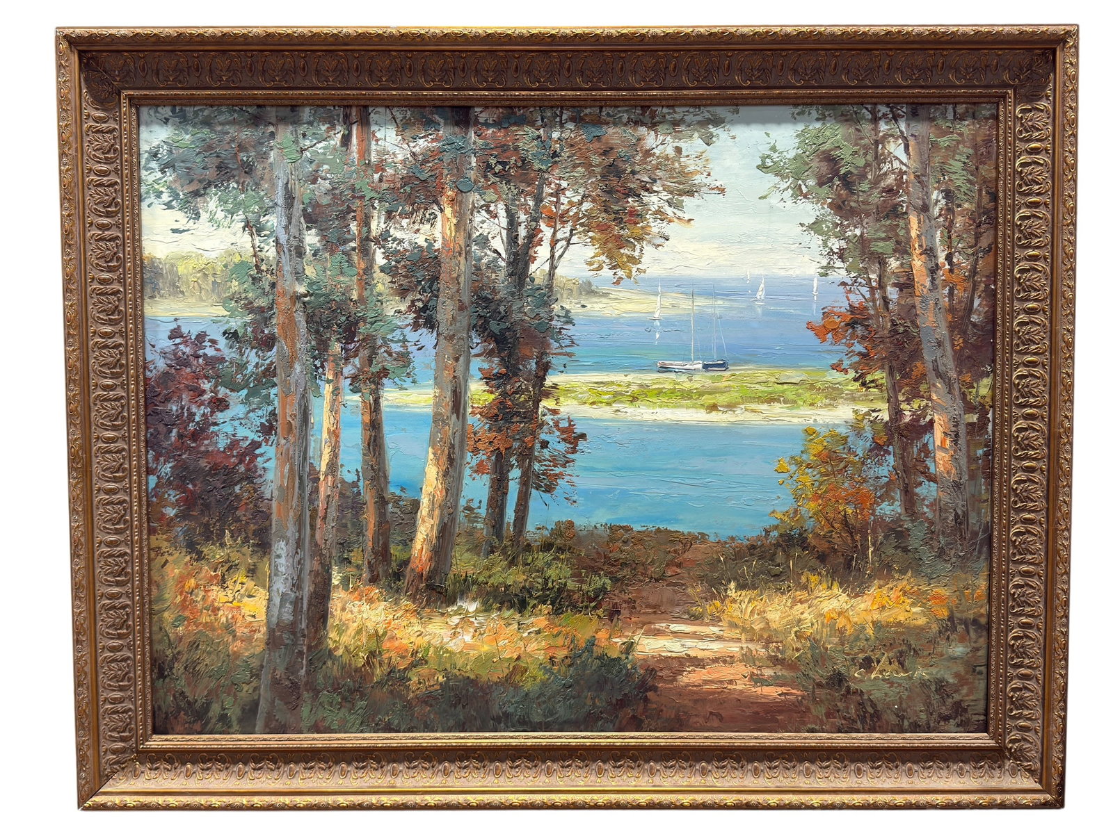 Large Oil on Canvas Wooded Lakeside Landscape w/ Sailboats: Large decorative oil on canvas landscape depicting a wooded overlook opening onto a vivid blue lake or coastal inlet, with tall trees framing the composition and a sunlit path leading toward the water