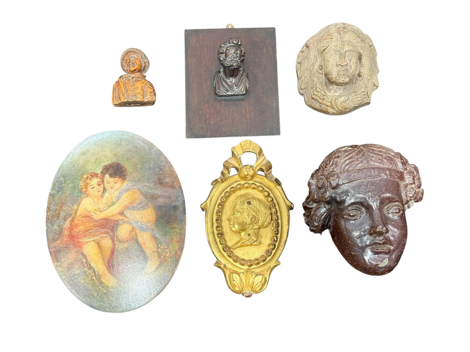 (6) Antique & Vintage Figural Wall Plaques & Carved Decorative Objects: Eclectic group of six antique and vintage decorative objects comprising three carved figural pieces, an oval painted plaque, a carved giltwood portrait medallion, and a sculpted cement face plaque. Th