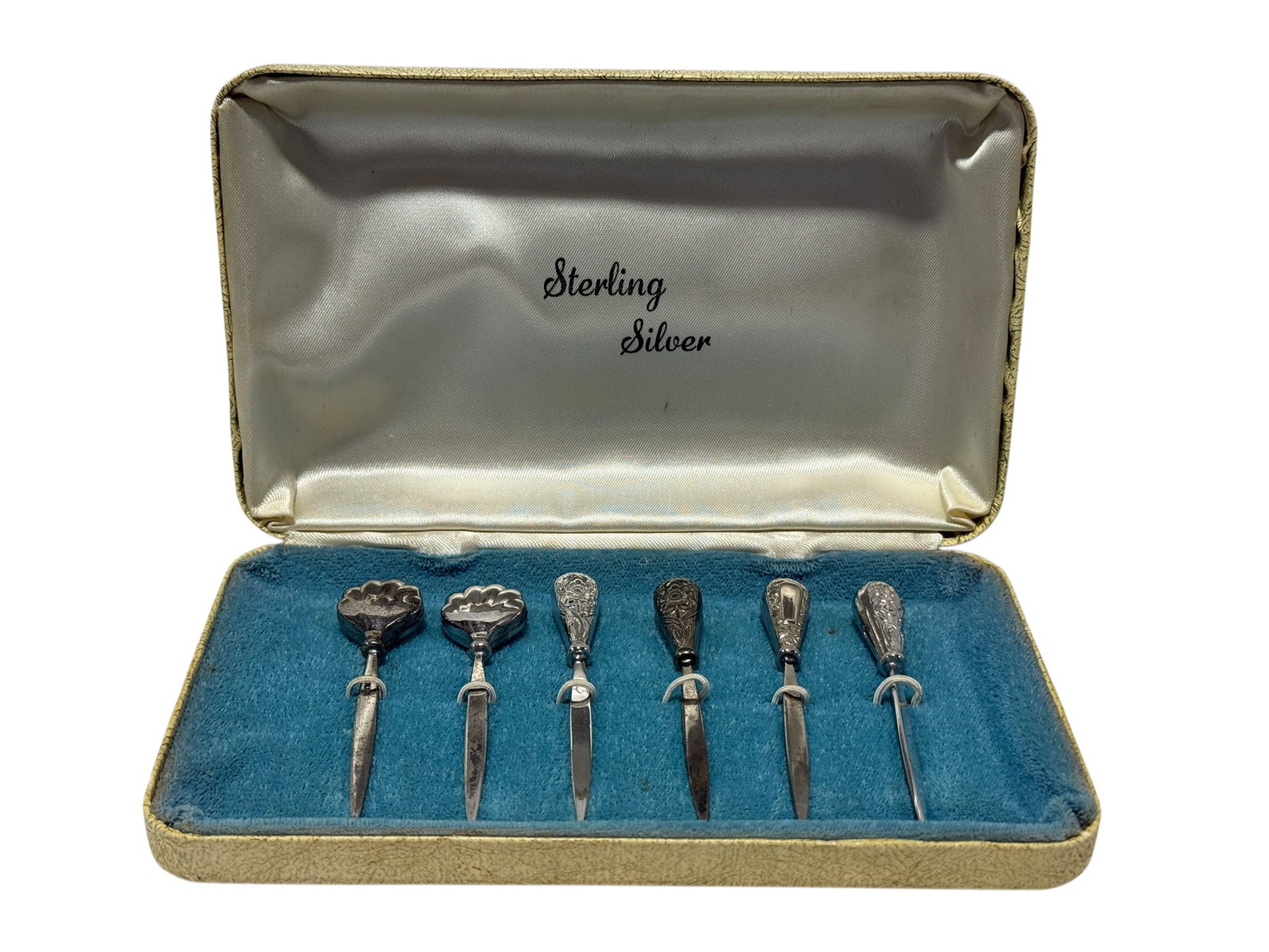 (6) Sterling Silver Cocktail Picks in Fitted Case: Six decorative sterling silver cocktail or hors d’oeuvre picks, each fitted with an ornate sterling handle featuring varied floral, foliate, and shell-form decoration above a slender pointed pick. A
