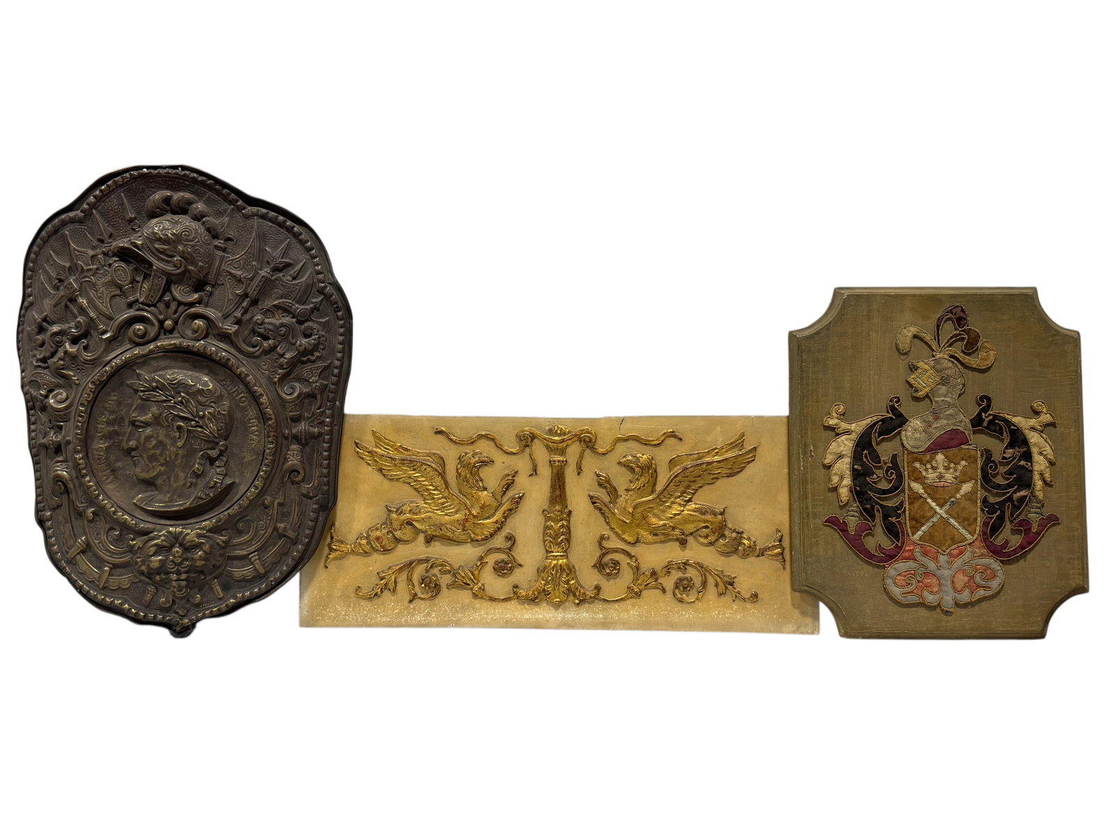 Group of 3 Antique & Vintage European Decorative Wall Plaques: An eclectic group of three European decorative wall plaques displaying heraldic, Renaissance Revival, and classical motifs. The group includes an ornate cast metal plaque centered by a profile portrai