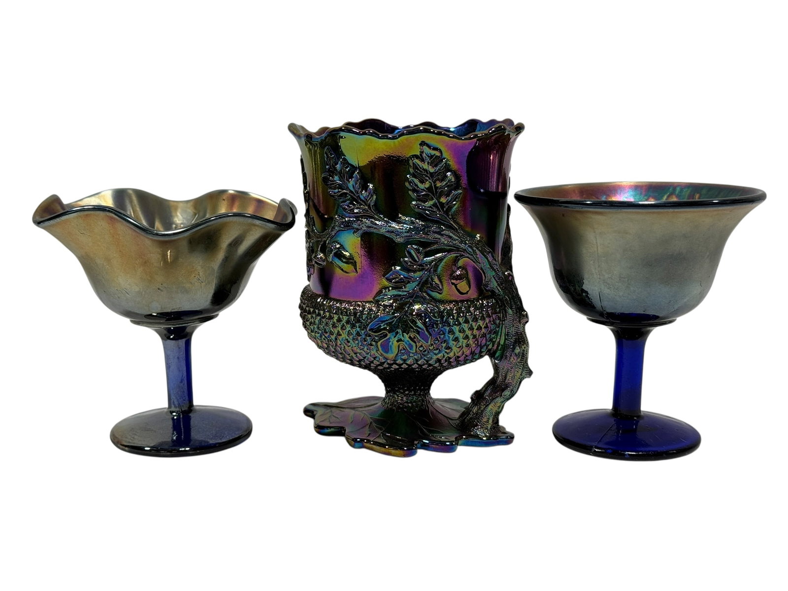 (3) Vintage Iridescent Carnival Glass Pedestal Pieces: A colorful three-piece grouping of vintage iridescent carnival glass comprising two footed compote-style bowls and an ornate acorn-and-oak-leaf vase. The two pedestal bowls are formed with deep cobalt