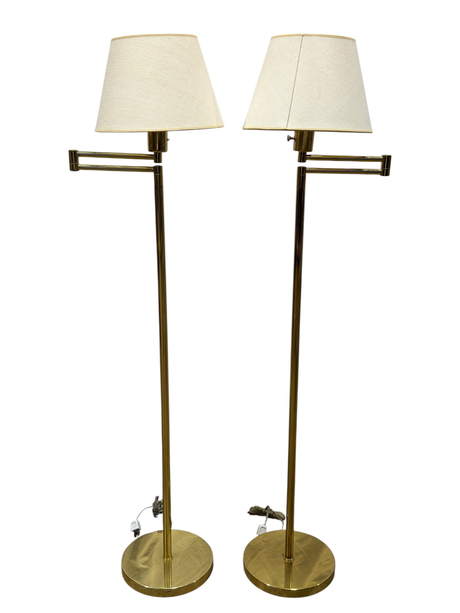 Pair of Mid Century Brass Swing Arm Floor Lamps: Pair of mid-century style brass floor lamps, each designed with a tall slender standard rising from a broad circular weighted base and fitted with a double-jointed swing arm that allows the light to e