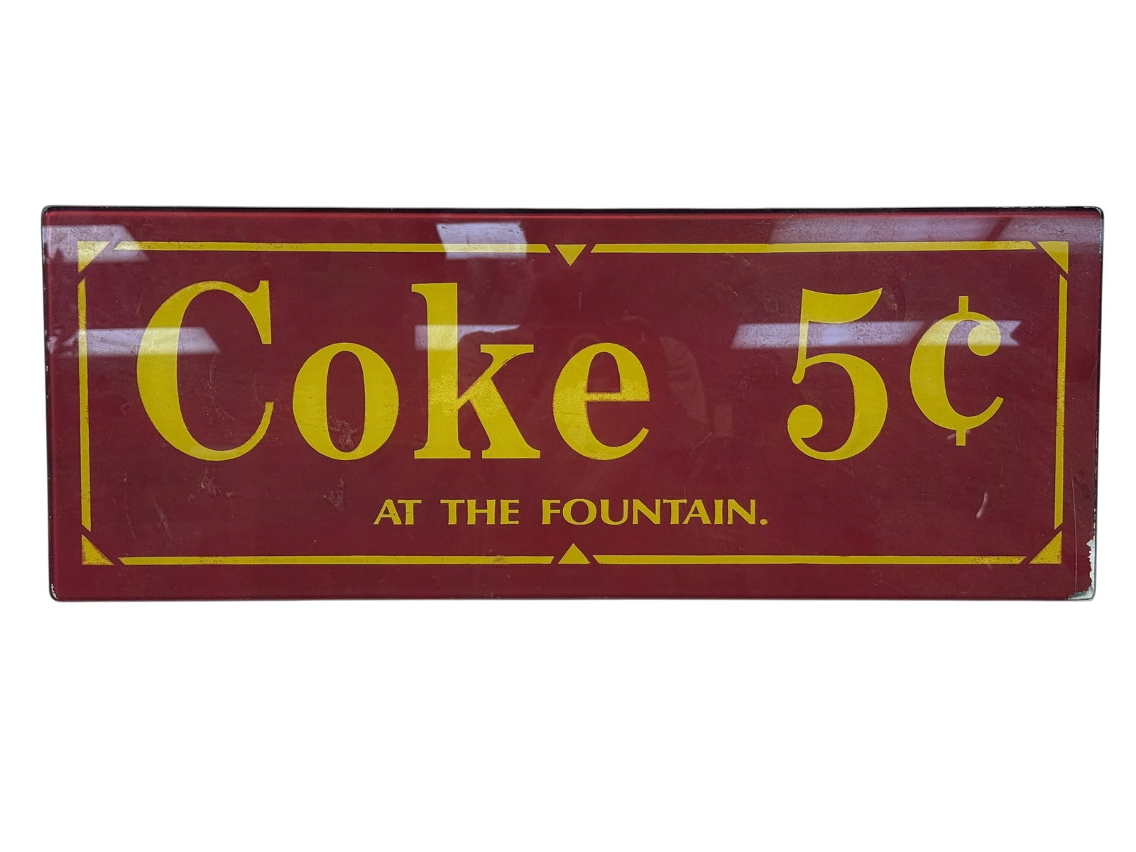 Vintage "Coke 5¢ at the Fountain" Reverse Painted Glass Advertising Sign: Vintage rectangular reverse-painted glass advertising sign featuring a deep red ground with bold yellow lettering reading “Coke 5¢ at the Fountain.” The graphic is applied to the reverse of t