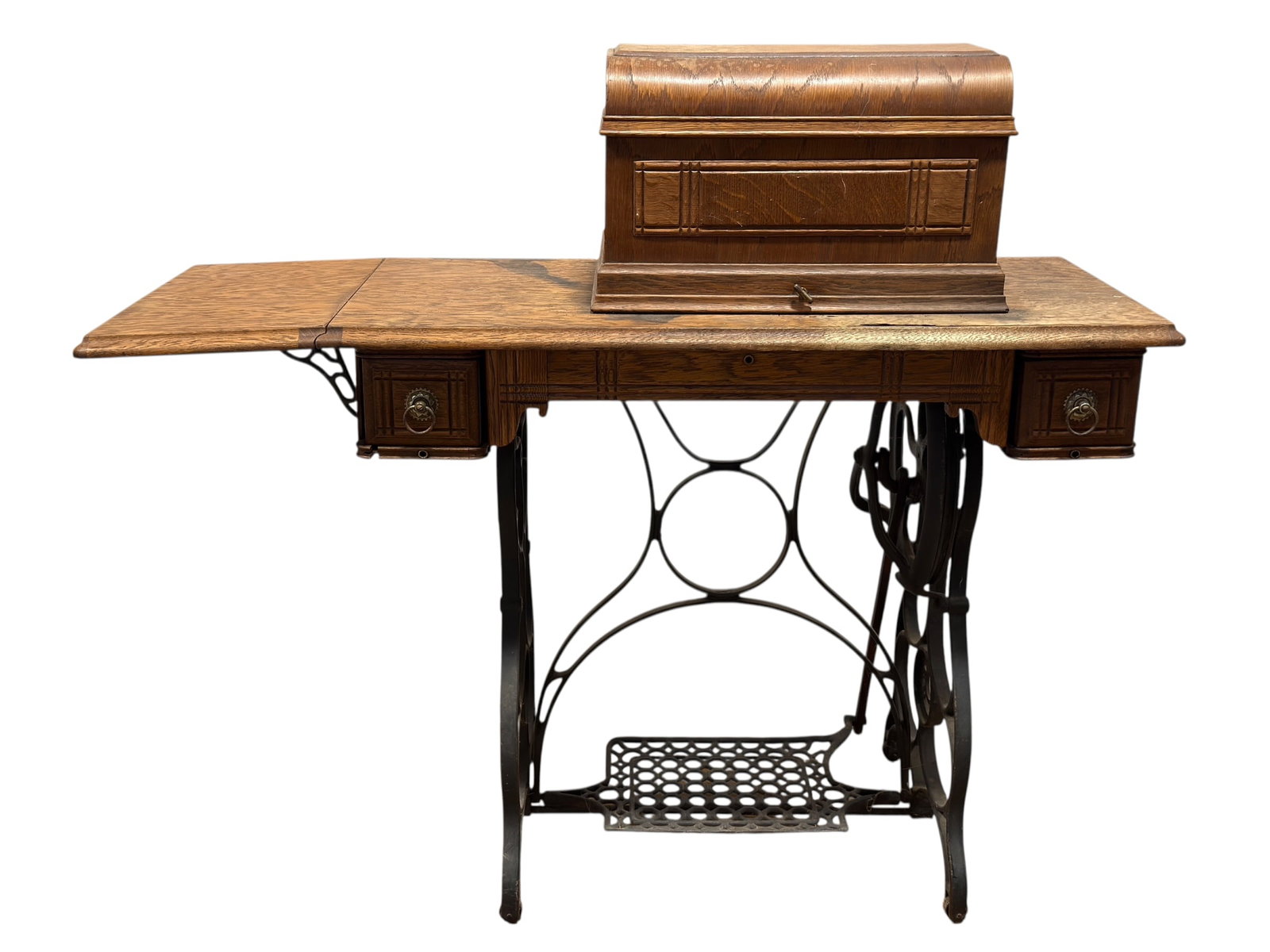 Antique New Home Treadle Sewing Machine in Oak Cabinet w/ Attachments: Early 20th-century New Home treadle sewing machine mounted in a quarter-sawn oak cabinet with fold-out work surface, carved drawer fronts, cast-iron treadle base, large drive wheel, and decorative pie