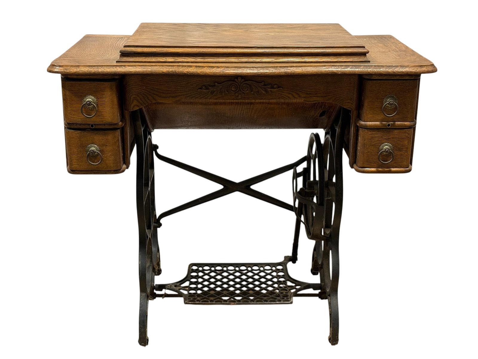 Antique Treadle Sewing Machine in Oak Cabinet: Antique treadle-operated sewing machine housed in a substantial oak cabinet with a hinged work surface, decorative carved apron, four small side drawers fitted with ring pulls, and a black cast-iron t
