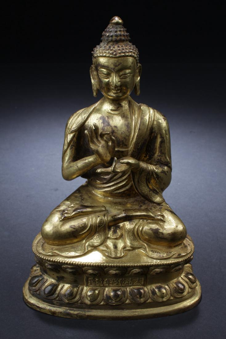 Chinese Gilt Bronze Buddha Statue: Seated in dhyanasana on a double-lotus throne, the hands in mudra, wearing flowing robe, with pendulous earlobes, the face with a serene expression. A seven chinese characted is imprinted at the thron