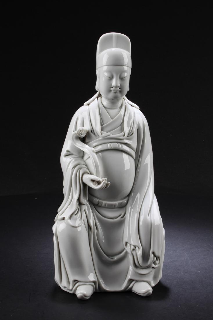 A Chinese Blanc De Chine Statue: A Chinese Blanc De Chine Statue, depicting a sitting deity holding a ruyi scepter with the right hand and left hand resting on the lap, wearing long flowing robe and a hat. Height: 11.25"