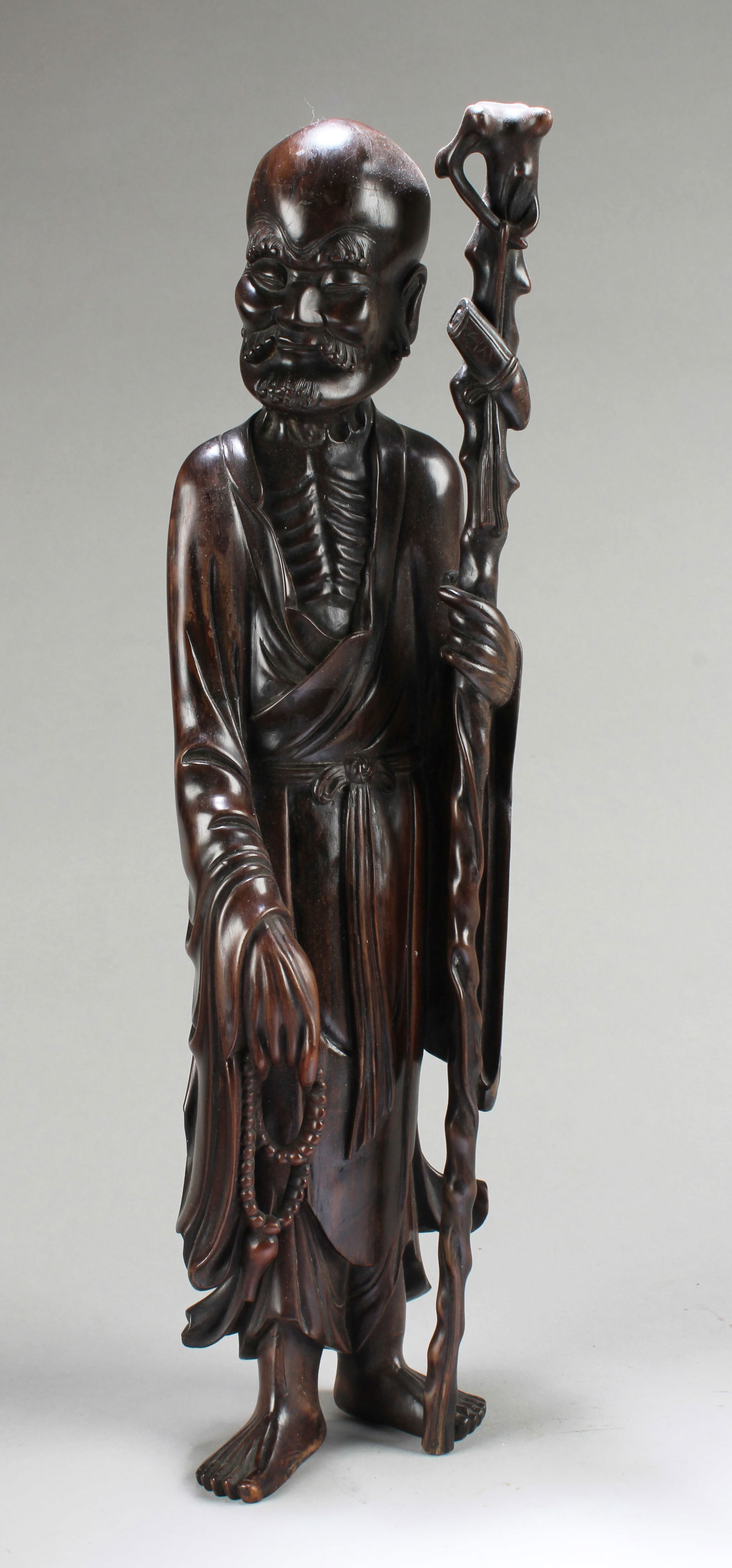 Antique Chinese Bowood Carved Statue: Antique Chinese Bowood Carved Statue, depicting a luohan wearing flowing robes, left hand holding a walking stick and right hand holding prayer beads.Height: 19.5"
