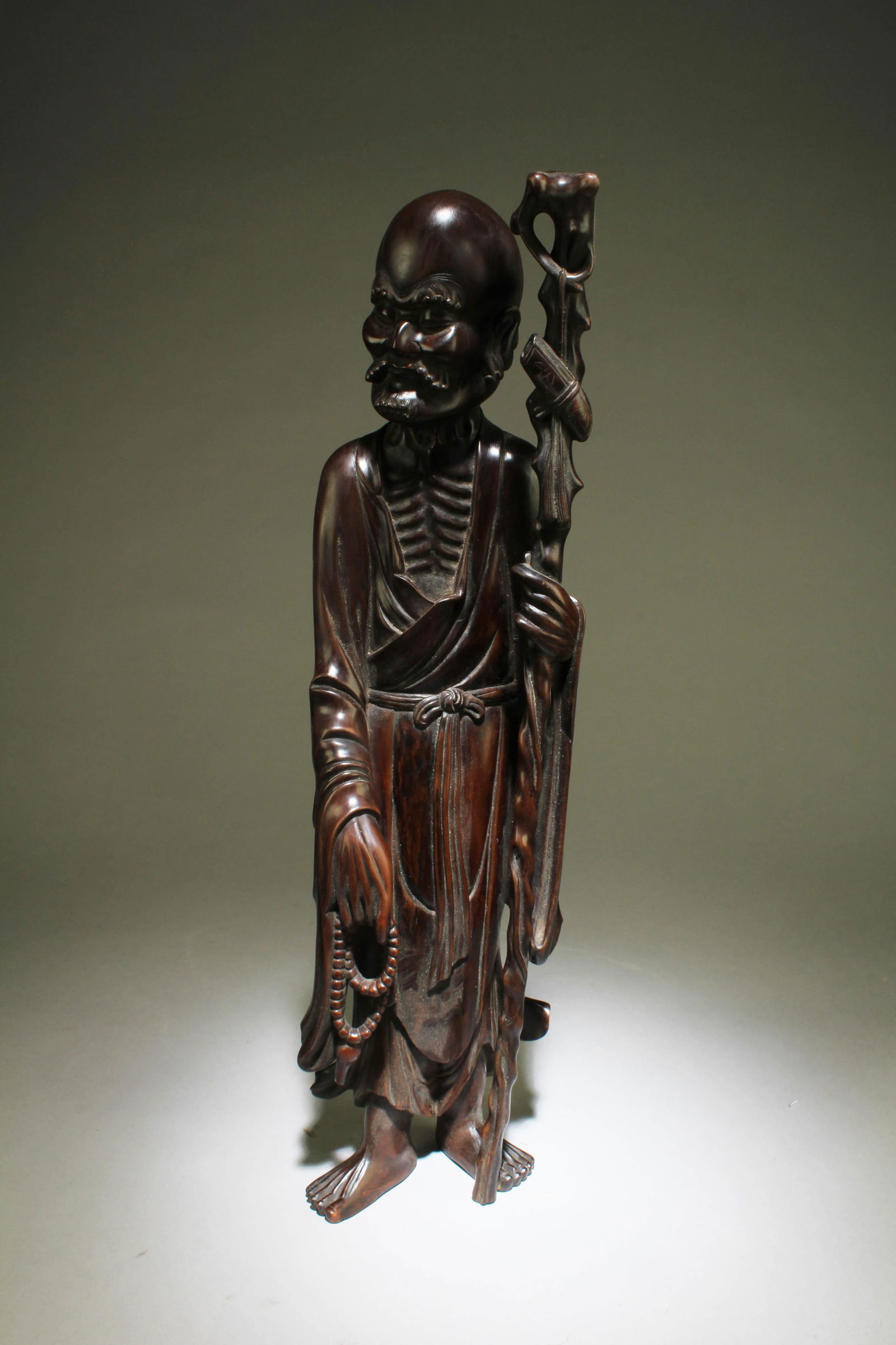 Antique Chinese Bowood Carved Statue: Antique Chinese Bowood Carved Statue, depicting a luohan wearing flowing robes, left hand holding a walking stick and right hand holding prayer beads.Height: 19.5"