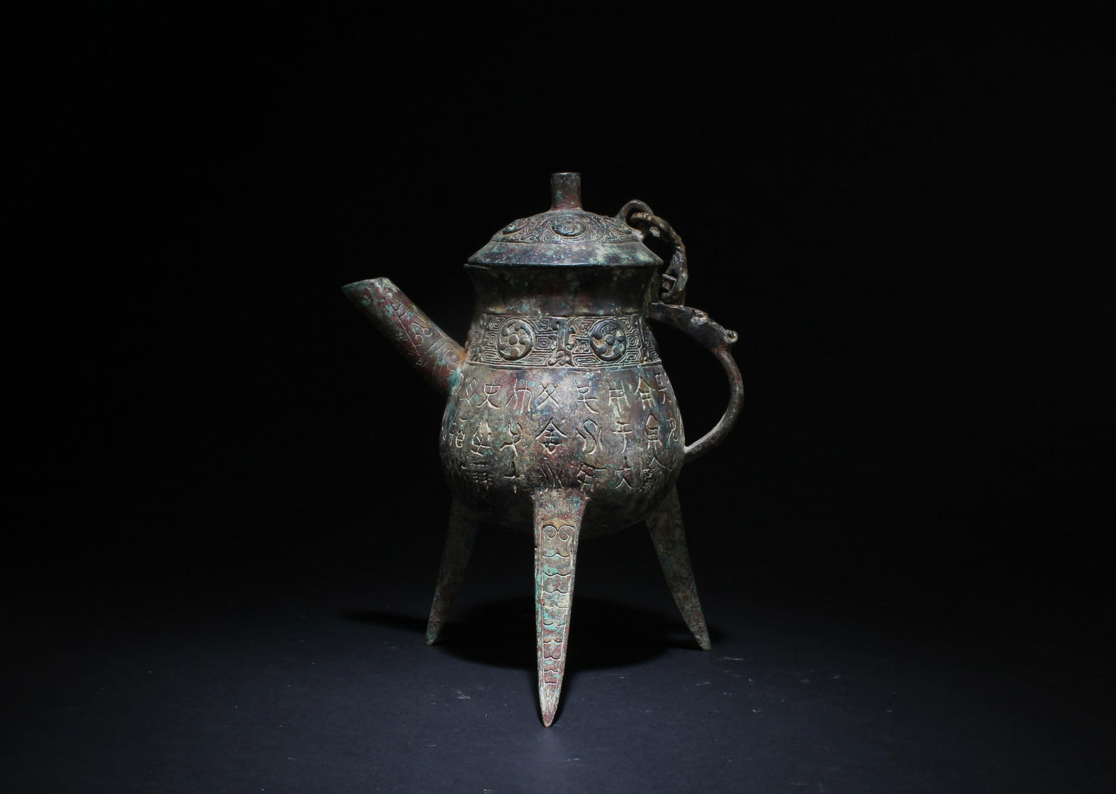 A Chinese Bronze Three-Legged Wine Pot: A Chinese Bronze Three-Legged Wine Pot with Inscribed Characters Chinese. Dimensions: 8.5" x 7.5".