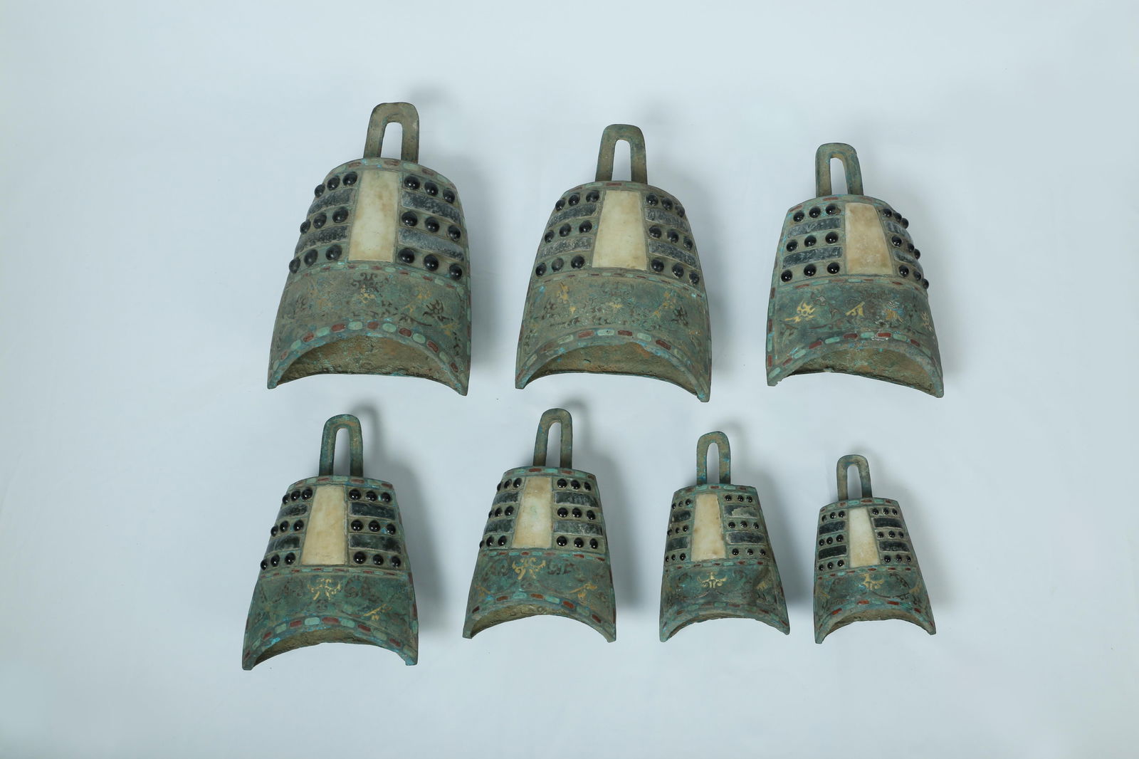 A Group of Seven Bronze Bells: A Group of Seven Bronze Bells, with jadestone and semi-precious stones inlaid, gold-inlay pattern. Dimension: 26.5 cm x 16.5 cm x 10.2 cm (Largest)