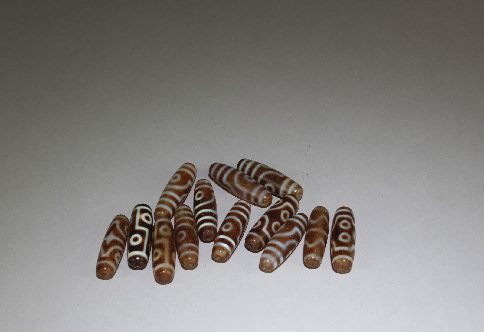 A Group of Thirteen Dzi Beads: A Group of Thirteen Dzi Beads. Length: 1.5'' (Approx)