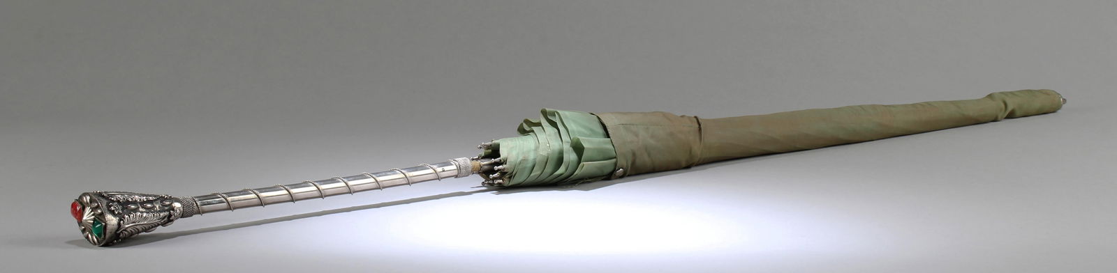 ANTIQUE STERLING SILVER EMBELLISHED UMBRELLA: The handle cast in relief with raised motif and embellished with gem-like decorations. Length: 34"