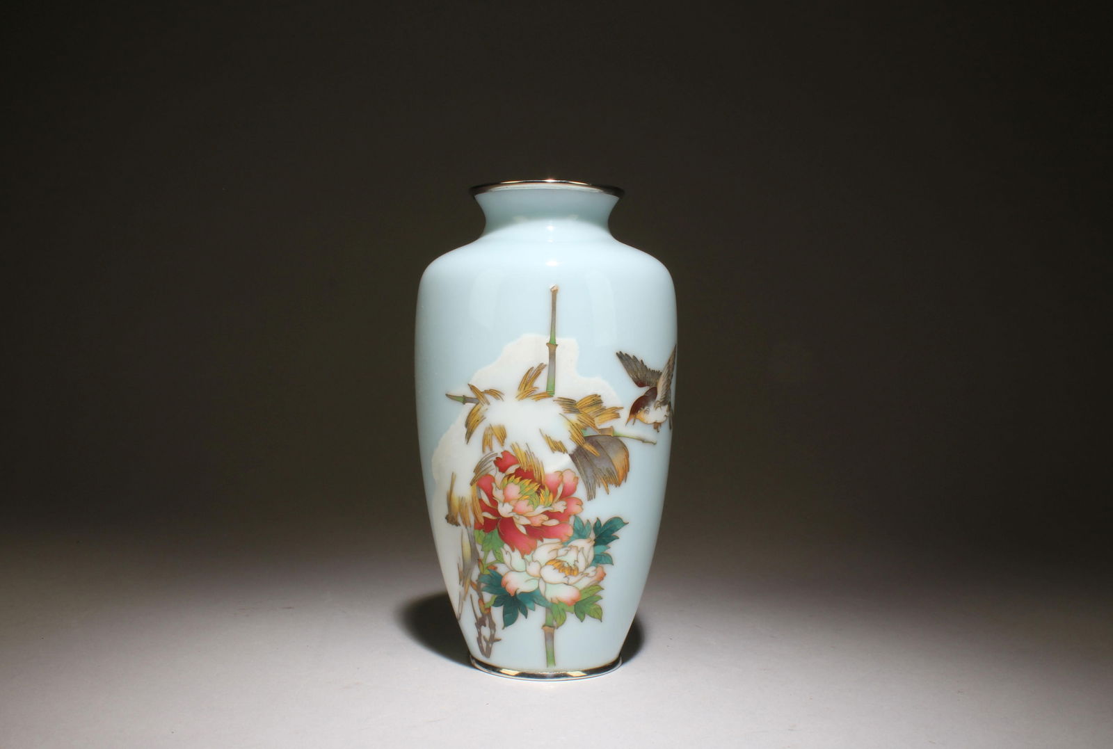 Meiji Cherry Pale Blue Enamel Cloisonne Vase: Meiji Cherry Blossom Pale Blue Enamel Base Cloisonne Vase. Dimensions: 7.25''x4''. It is a cloisonne vase with a gold rim. The vase has a floral design on it with red, pink, and white flowers and