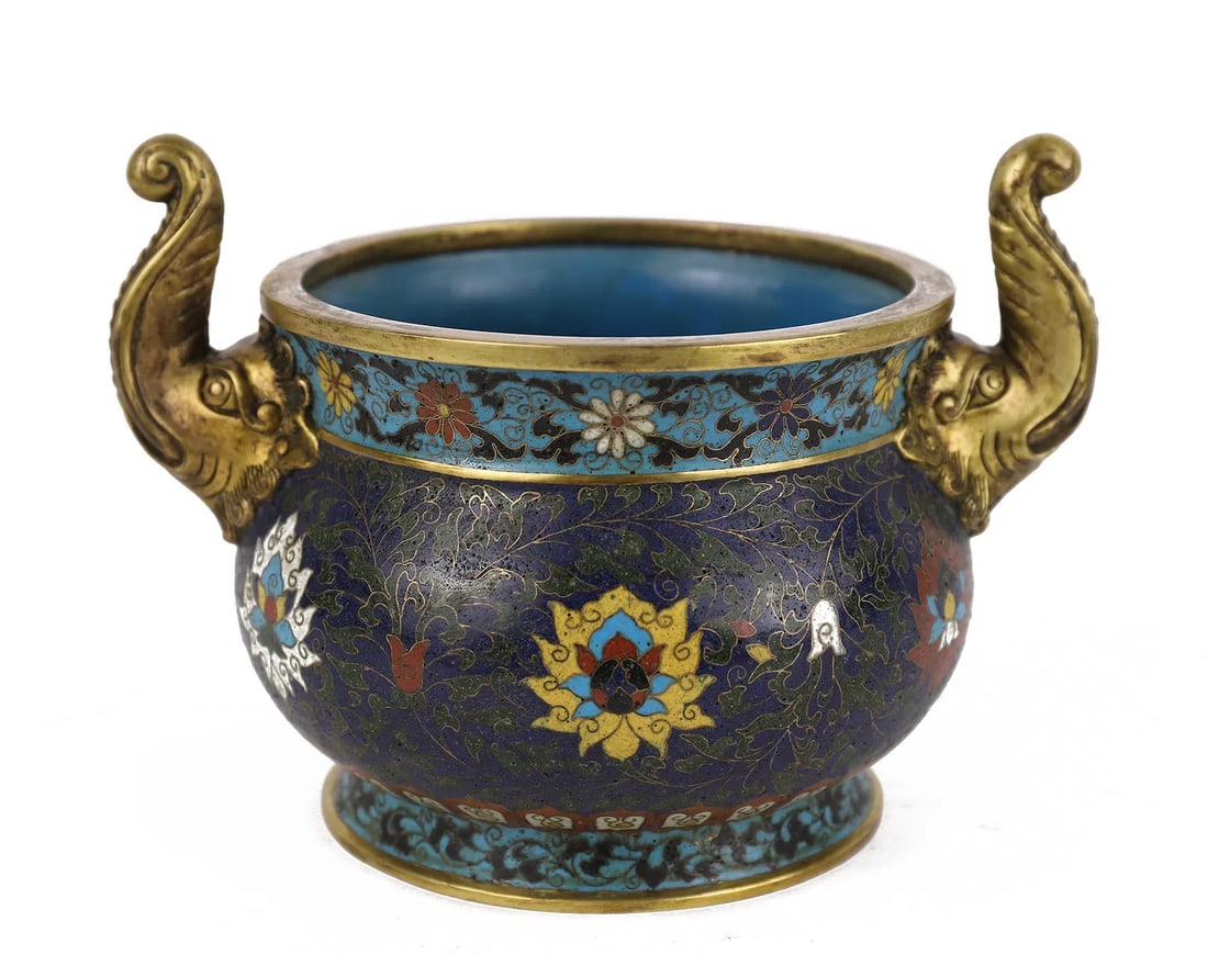 A CHINESE CLOISONNE ENAMEL CENSER: Measurements: L. 22 cm. W. 17 cm. H. 15 cm. The compressed globular censer is supported on a circular foot and the sides are cast with two elephants handles, decorated with lotus flowers and