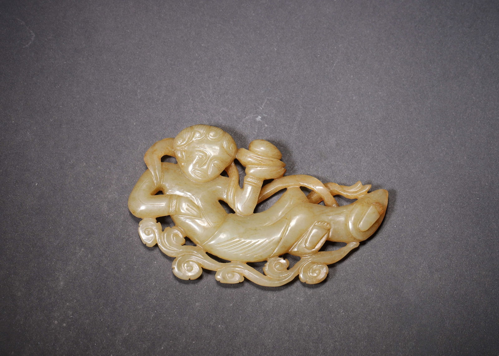 MING DYNASTY GREENISH YELLOW JADE OPENWORK FLYING APSARAS OFFERING TREASURE PENDANT: 3.62in x 2.24in (9.2cm x 5.7cm) | 0.143lbs (65g)A fine Ming Dynasty greenish yellow jade openwork pendant, depicting a flying apsaras offering a treasure box, with flowing ribbons and scrolling clouds