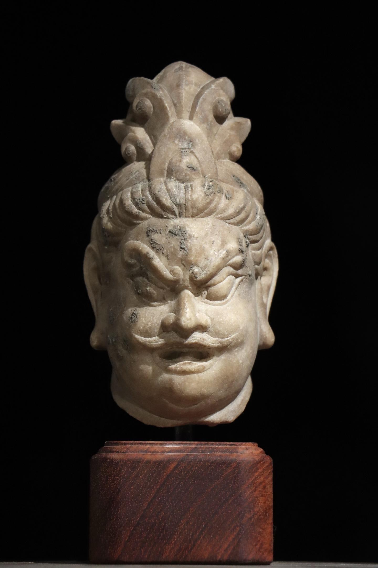 A TANG DYNASTY WHITE MARBLE STATUE OF A STRONGMAN'S HEAD: H:22cm(8.66in) H:16cm(6.30in)Weight:15000gA white marble stone head of heavenly guardian warrior, with a fierce and dignified countenance, scroll cloud crown, raised brows and moustache, smooth stone 