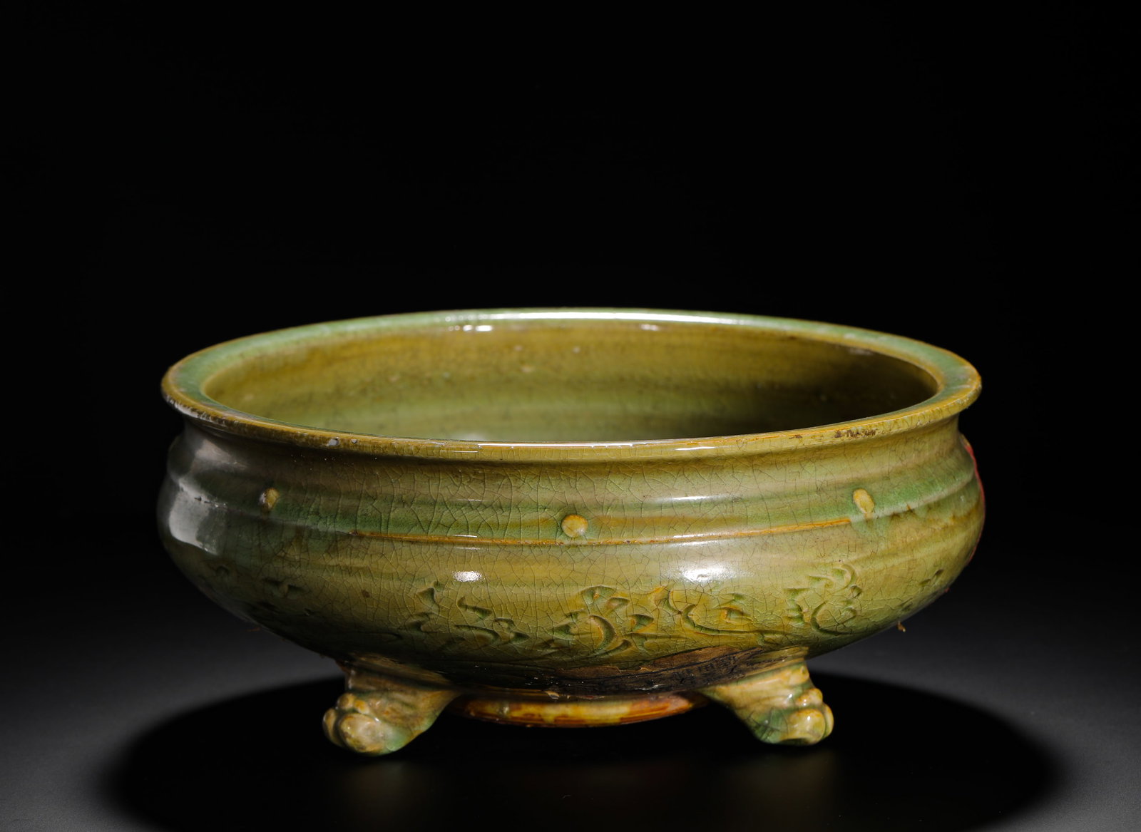 A BLUE GLAZED THREE-LEGGED FURNACE ENGRAVED WITH FLORAL PATTERNS FROM THE MING LONGQUAN KILN: H:11cm (4.33in) D:26cm (10.24in) Weight:1850g (4.08lb) This is a Ming Dynasty porcelain censer from the Longquan Kiln. It is covered in a rich, jade-like celadon glaze with floral patterns carved on t