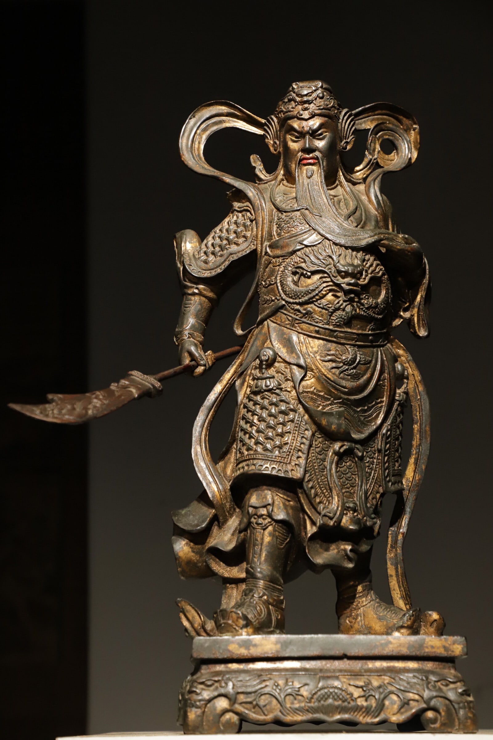A STANDING BRONZE STATUE OF GUAN GONG FROM THE MING DYNASTY: Weight:17000g=17.00kg(37.41lb);H:56cm(22.05in) L:22cm(8.66in) W:20cm(7.87in)A gilded bronze standing statue of Guan Gong, clad in dragon-patterned fish-scale armor and holding a green-dragon crescent 