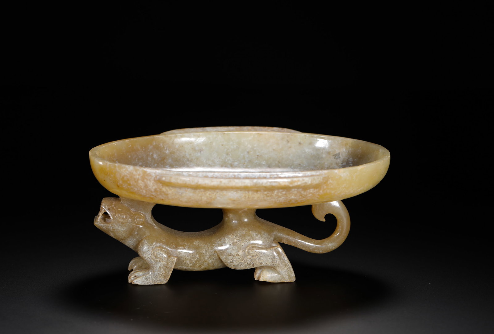 HAN DYNASTY HETIAN JADE BEAST FOOT HIGH FOOT PLATE: H:5.5cm(2.17in) W:13.5cm(5.32in) Weight:250g(0.55lb)This is a Han Dynasty celadon jade stemmed dish, supported by a striding mythical beast, showcasing sophisticated craftsmanship and natural patina. 