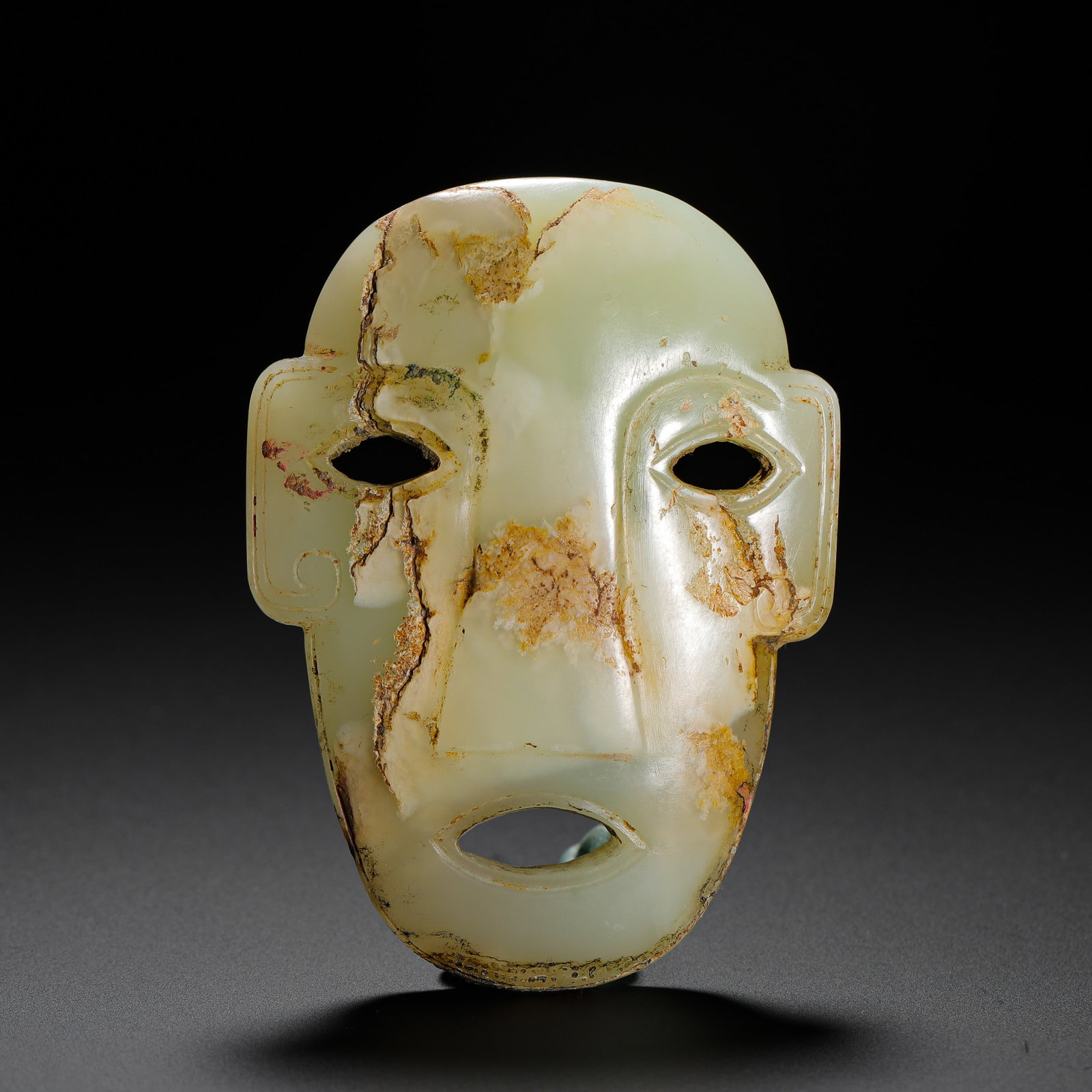 JADE FACE PENDANT OF THE SHANG DYNASTY: H:7.5cm (2.95in) W:5.8cm (2.28in) Weight:70g (0.15lb)A hidden threading hole is usually carved on the reverse for cord attachment to wear on the body. Ancients believed jade face masks could ward off 