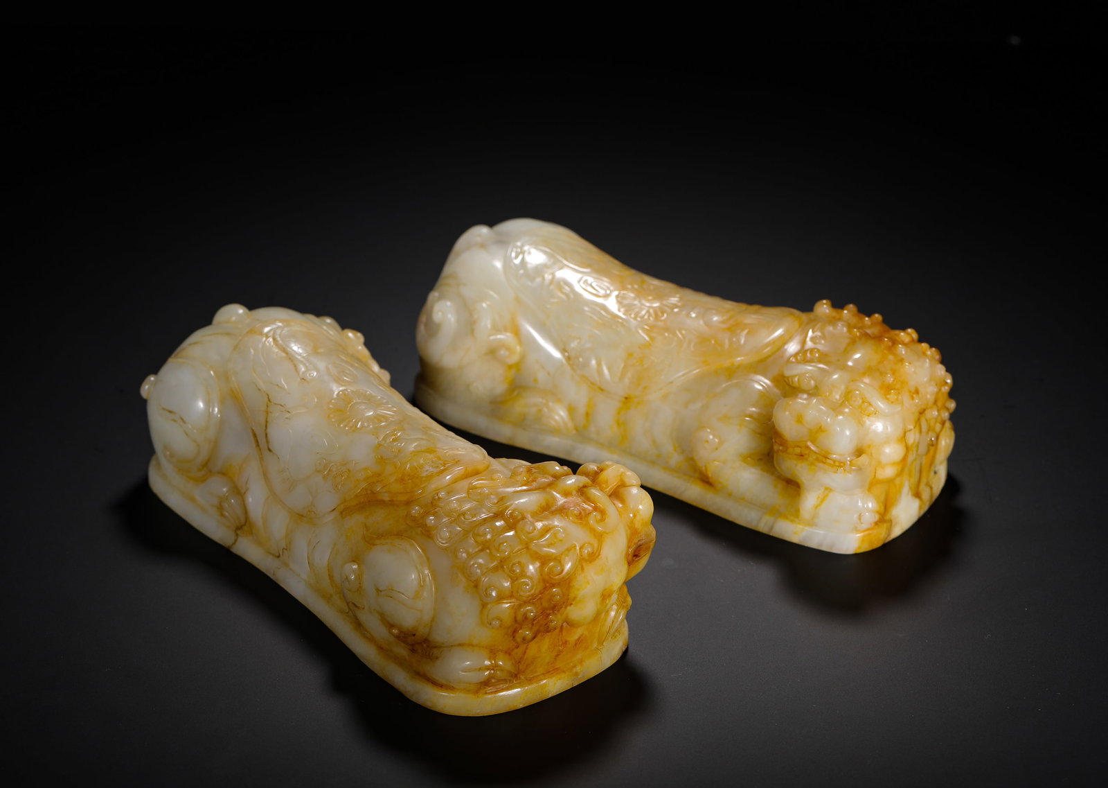 QING DYNASTY HETIAN JADE LUSTROUS LION-SHAPED PAPERWEIGHT: H:6.5cm (2.56in) W:20.8cm (8.19in) Weight:2730g (6.02lb)This is a pair of Qing Dynasty Hetian jade lion-form paperweights, with natural yellowish-brown patina, carved in the round as recumbent lions w