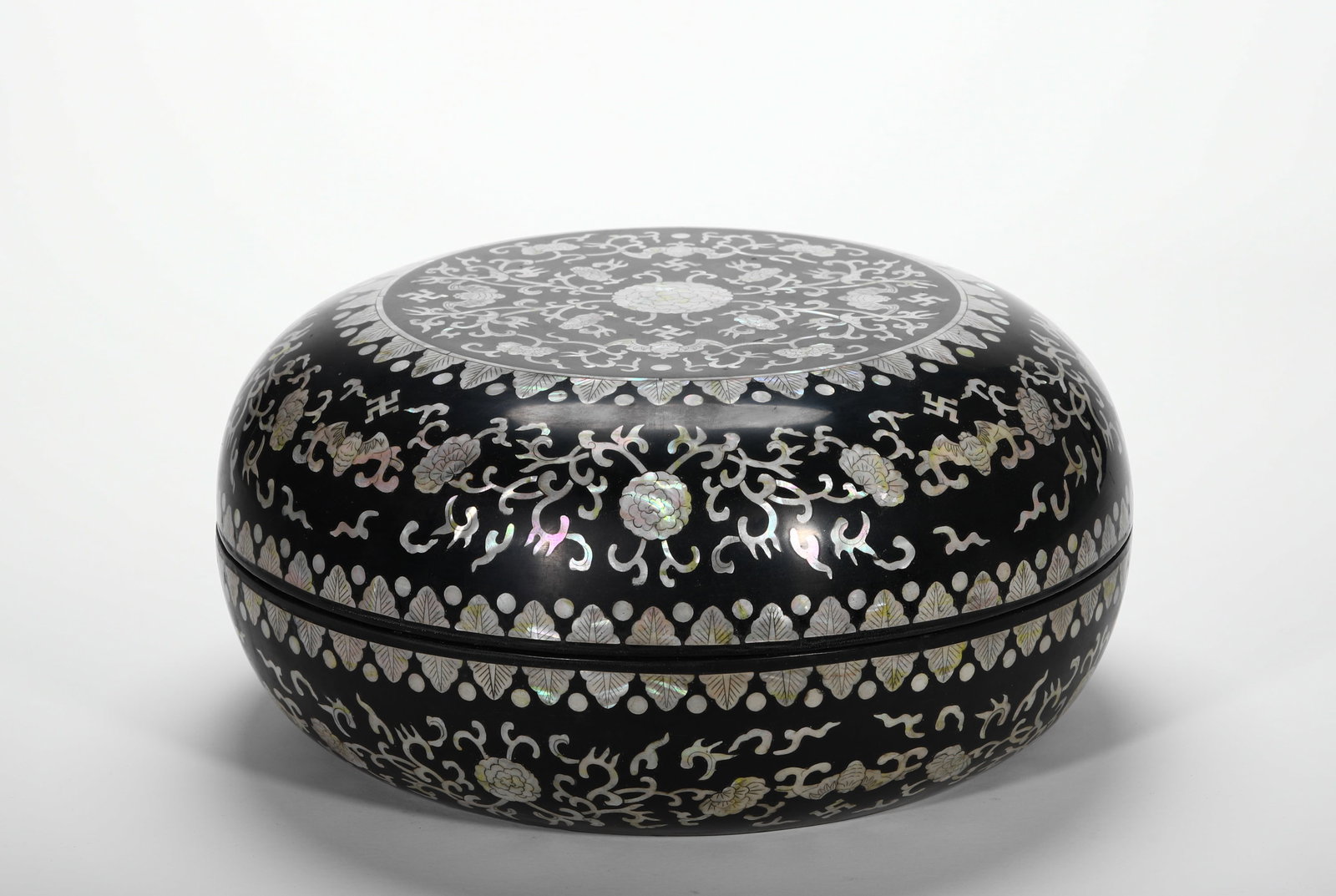 QING DYNASTY BLACK LACQUERED MOTHER-OF-PEARL INLAID LOTUS SWASTIKA ROUND CASE: H:16cm (6.30in) D:32cm (12.60in) Weight:1450g (3.20lb)Wood-cored lacquer container fully inlaid with iridescent shell foliage and Buddhist symbols.