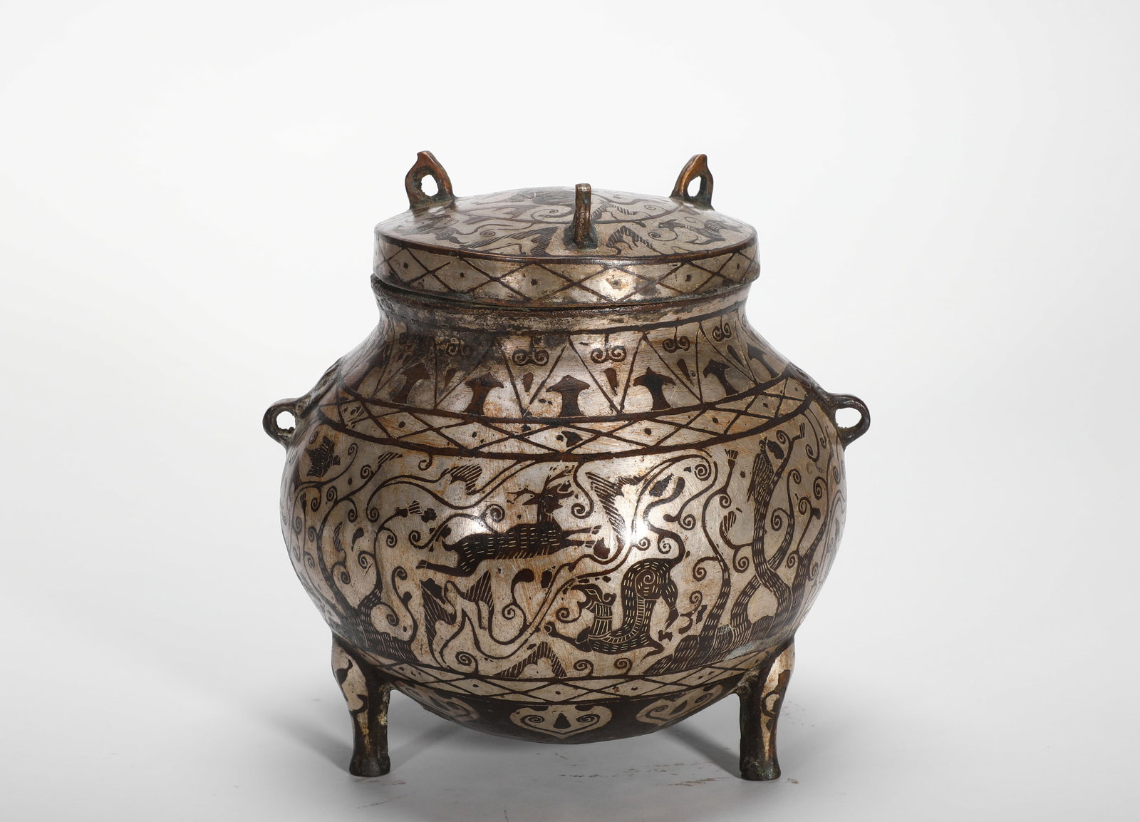 BRONZE INLAID SILVER HUNTING PATTERN THREE-LEGGED LID JAR OF THE HAN DYNASTY: H:17cm(6.69in)W:12.5cm(4.92in)Weight:1570g(3.46lb)This is an outstanding example of bronze craftsmanship from the Warring States to Han period, used by the nobility to hold food or wine.
