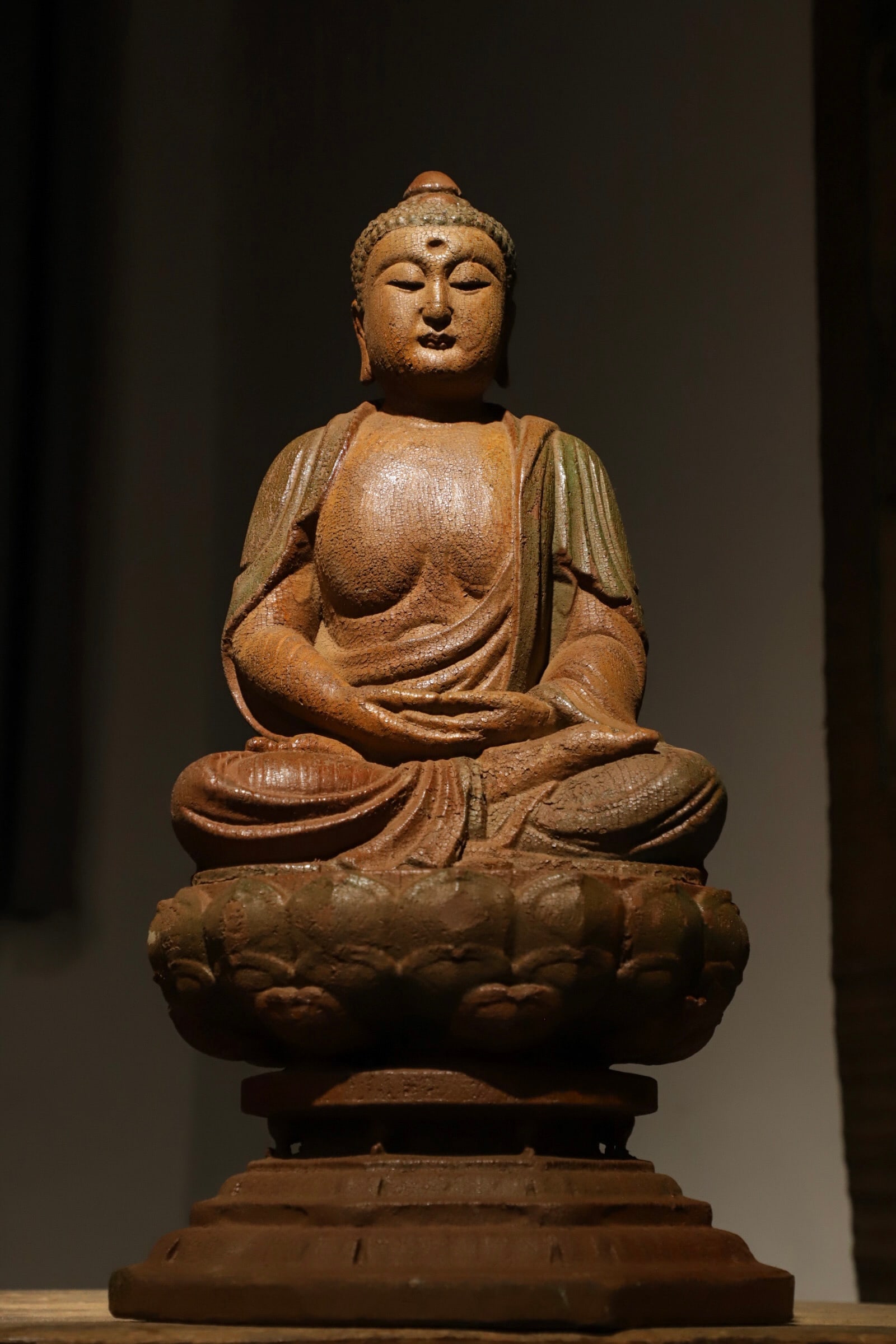 A MING DYNASTY WOODCARVING OF SAKYAMUNI SITTING IN MEDITATION: H:53cm (20.87in) L:27cm (10.63in) W:25cm (9.84in)Carved from single solid wood with partial surviving green mineral pigment; seated in full lotus posture on lotus throne atop double-tiered base, an an