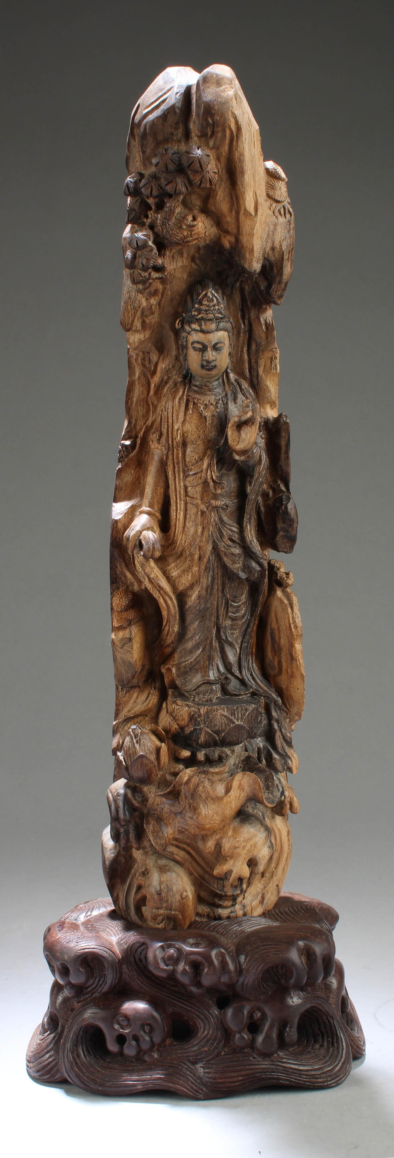 A Chinese Agarwood Carved Guanyin Statue: Standing on a lotus throne, hand in mudram the face with a serene expression. Comes fitted with a wooden stand. Height: 13.5"