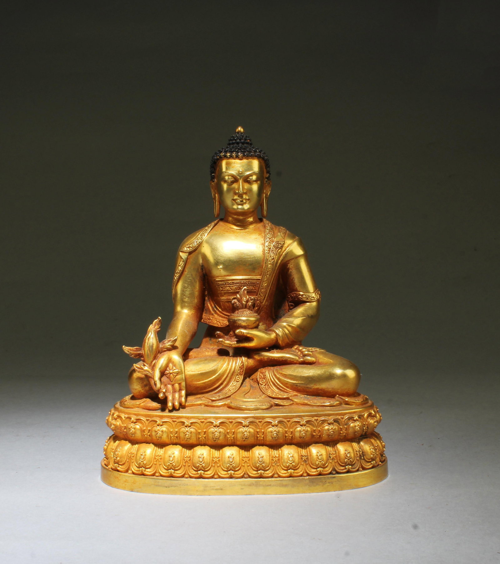 A Gilt Bronze Buddha Statue: Seated on a lotus base, left hand holding a religious item, and right hand resting on the lap with palm faced out, eyes with serene expression. 'YongLe' mark at the back. Height: 6.2"
