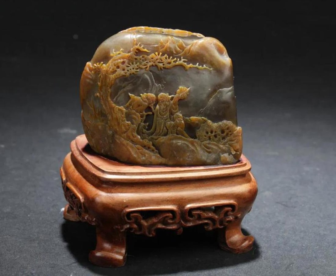 Chinese Soapstone Carved Ornament: Chinese Soapstone ornament, depicting carved in relief of immortals surrounded by mountain landscape. Comes fitted with a wooden stand. Height: 2"