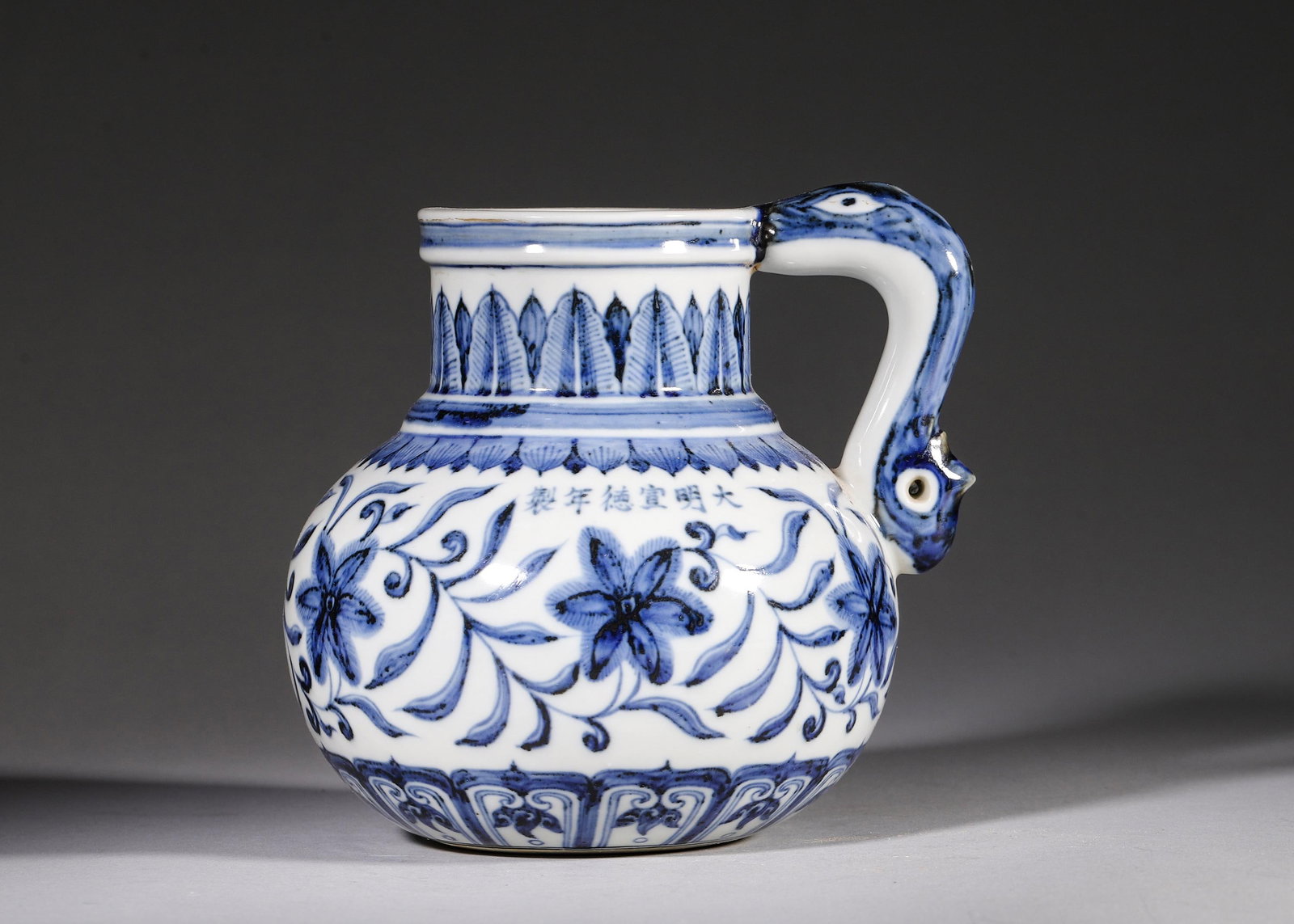 A BLUE AND WHITE DRAGON-HANDLED EWER WITH INTERLOCKING FLORAL PATTERN, MARK OF XUANDE, MING STYLE: W 15cm (5.91 in); H 14cm (5.51 in),This blue and white ewer has a straight neck, globular body and dragon-shaped handle. It is decorated with banana leaves, lotus petals and scrolling flowers, inscrib