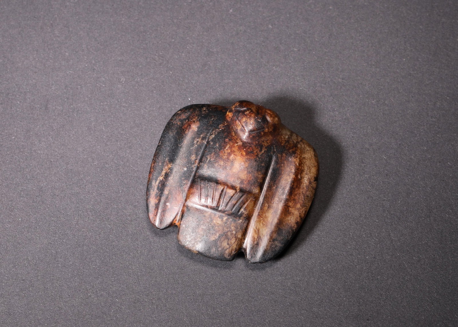 A Hongshan Culture Jade Owl Pendant, Neolithic Period: Wt 51.0g (0.11 lb); L 4.5cm (1.77 in); W 4.5cm (1.77 in); H 1.5cm (0.59 in)A Neolithic Hongshan Culture jade owl pendant. Carved in a stylized bird form with simple yet elegant lines, it features natu