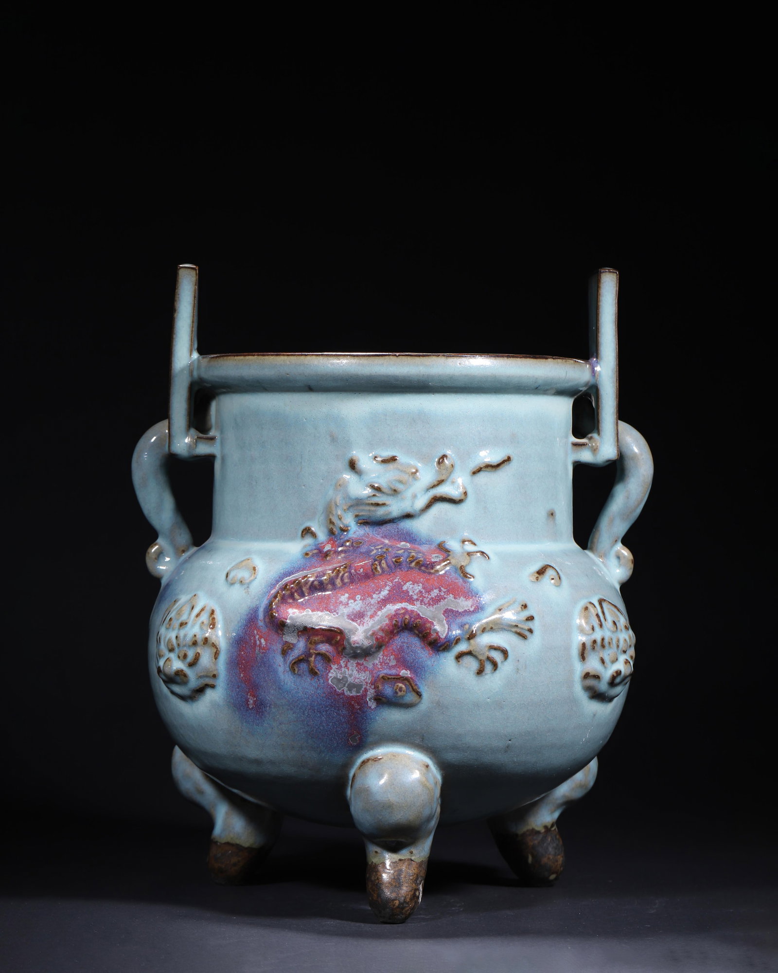 SONG DYNASTY JUN KILN SKY-BLUE GLAZED FLAMBE-GLAZED TRIPOD CENSER WITH APPLIED DRAGON AND BEAST MASK: 11.02in x 13.78in (28.0cm x 35.0cm)A fine Song Dynasty Jun kiln tripod censer, archaistic bronze ding form, with upright rectangular handles, applied dragon and beast mask reliefs. Covered in a sky-bl