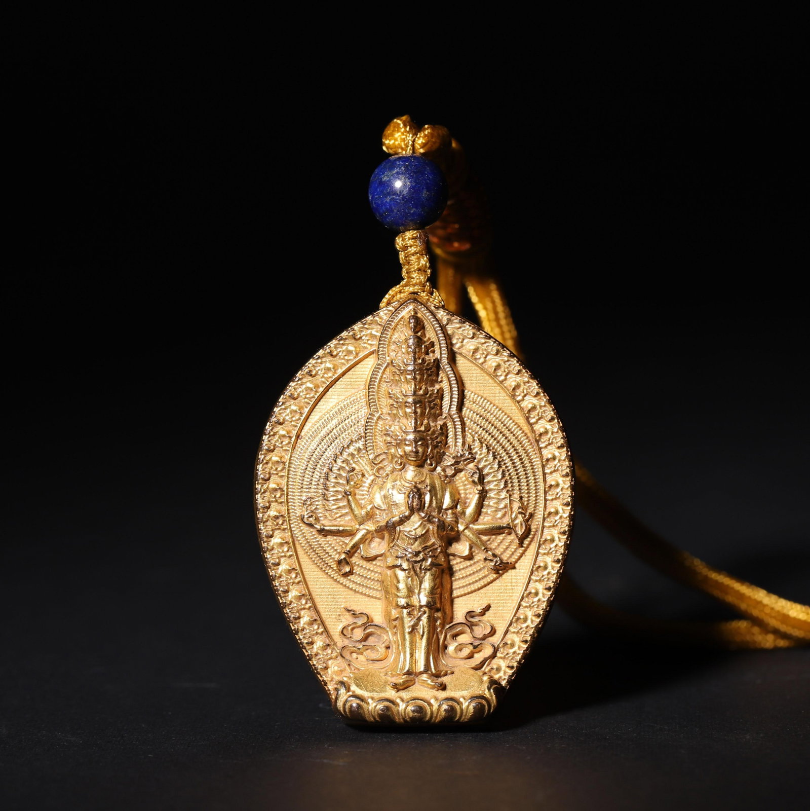 A Gilt Bronze Pendant of Thousand-Hand Guanyin, Xuande Period, Ming Dynasty: L 4.8cm (1.89 in); W 3.7cm (1.46 in); Wt 54g (0.12 lb)A gilt bronze pendant featuring a high-relief Thousand-Hand Guanyin on the obverse, with the deity in serene form, multiple arms outstretched, and