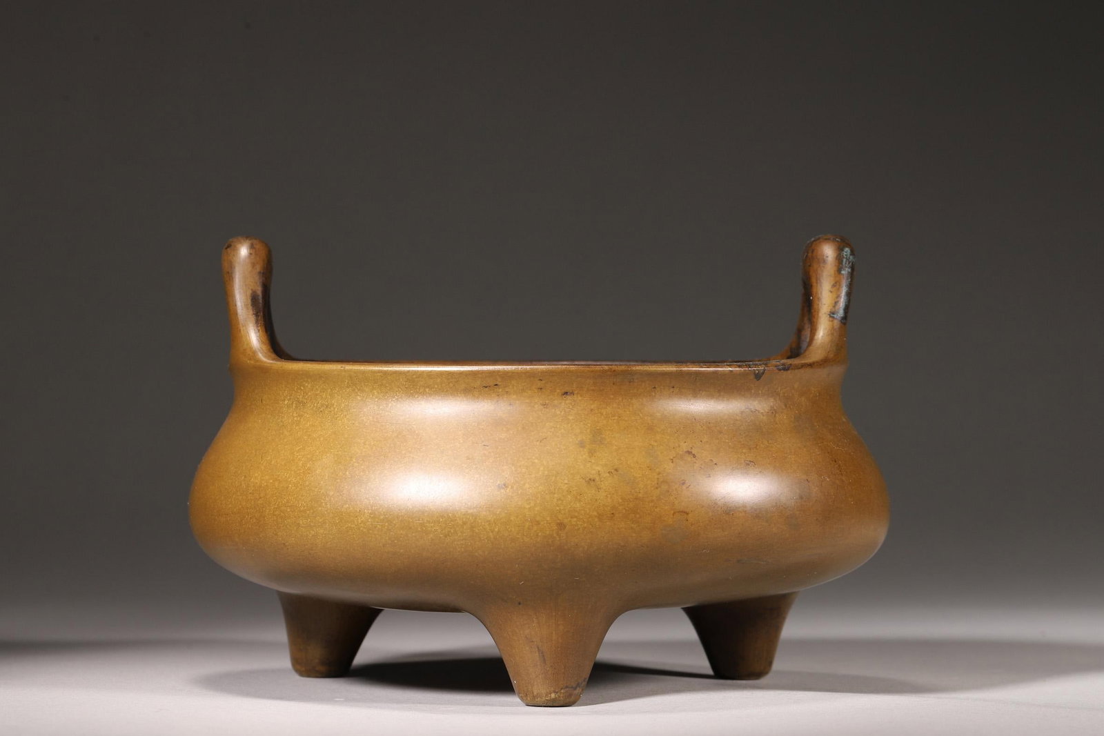 A Bronze Three-Foot Incense Burner with Bridge Handles, "Kangxi Renshen Ji Shi Jia Cang" Mark, Qing: Diameter 16.0cm (6.3in), Height 10.0cm (3.94in), Weight 1238.0g (2.73lb)A bronze three-foot incense burner with bridge handles, bearing the "Kangxi Renshen Ji Shi Jia Cang" mark, dating to the Qing Dy