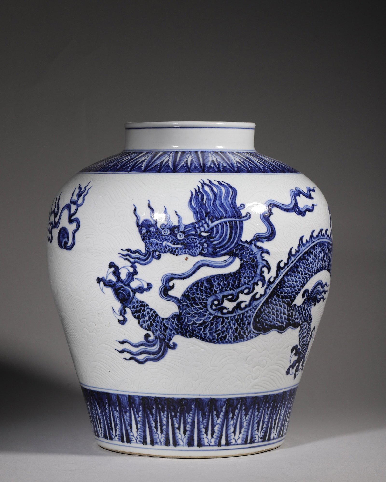 A BLUE AND WHITE PORCELAIN JAR WITH INCISED WAVE AND DRAGON MOTIF, YONGLE-XUANDE PERIOD, MING: L 29cm (11.42 in); H 35cm (13.78 in),Ming early blue and white jar with sand base, decorated with banana leaves on neck. Incised fine wave patterns as ground, overlaid with powerful five-claw dragon a