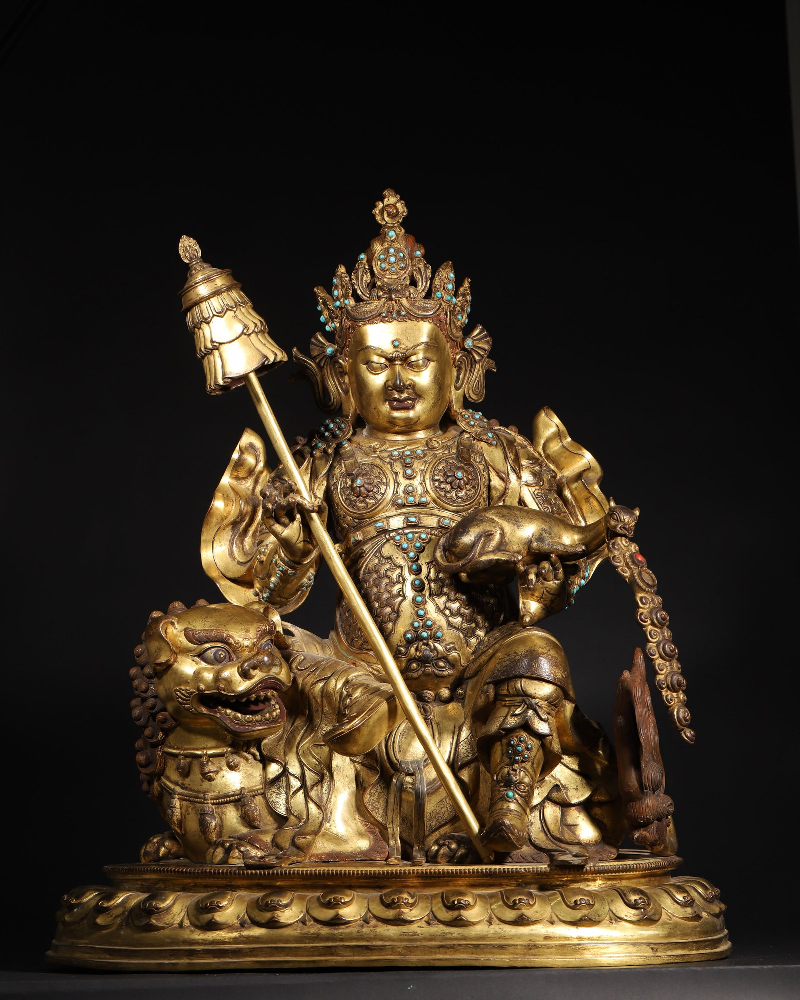 A FINE GILT-BRONZE GEM-INLAID FIGURE OF VAISHRAVANA, MID-QING DYNASTY: 22.05in x 14.17in x 25.59in (56.0cm x 36.0cm x 65.0cm), 59.525lb (27000.0g)This magnificent Mid-Qing gilt-bronze Vaishravana sits on a lion throne, holding a victory banner and a rat-spitter, inlaid w